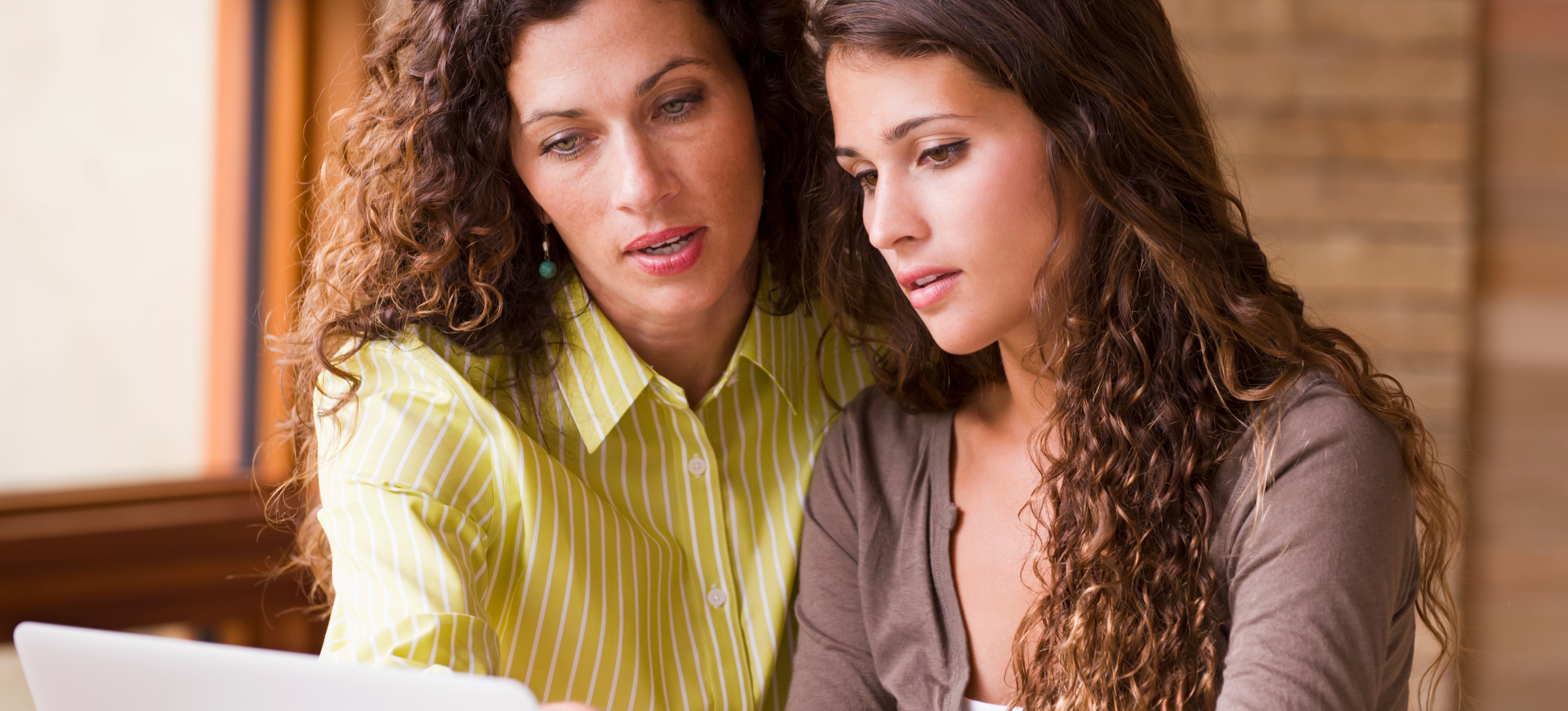 [Featured Image] A mother and daughter look at a laptop screen together as they try to figure out if colleges look at weighted or unweighted GPAs.
