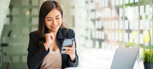[Image en vedette] Une ingénieure en informatique souriante tient un téléphone Android équipé d'un VPN APK alors qu'elle est assise à son bureau.