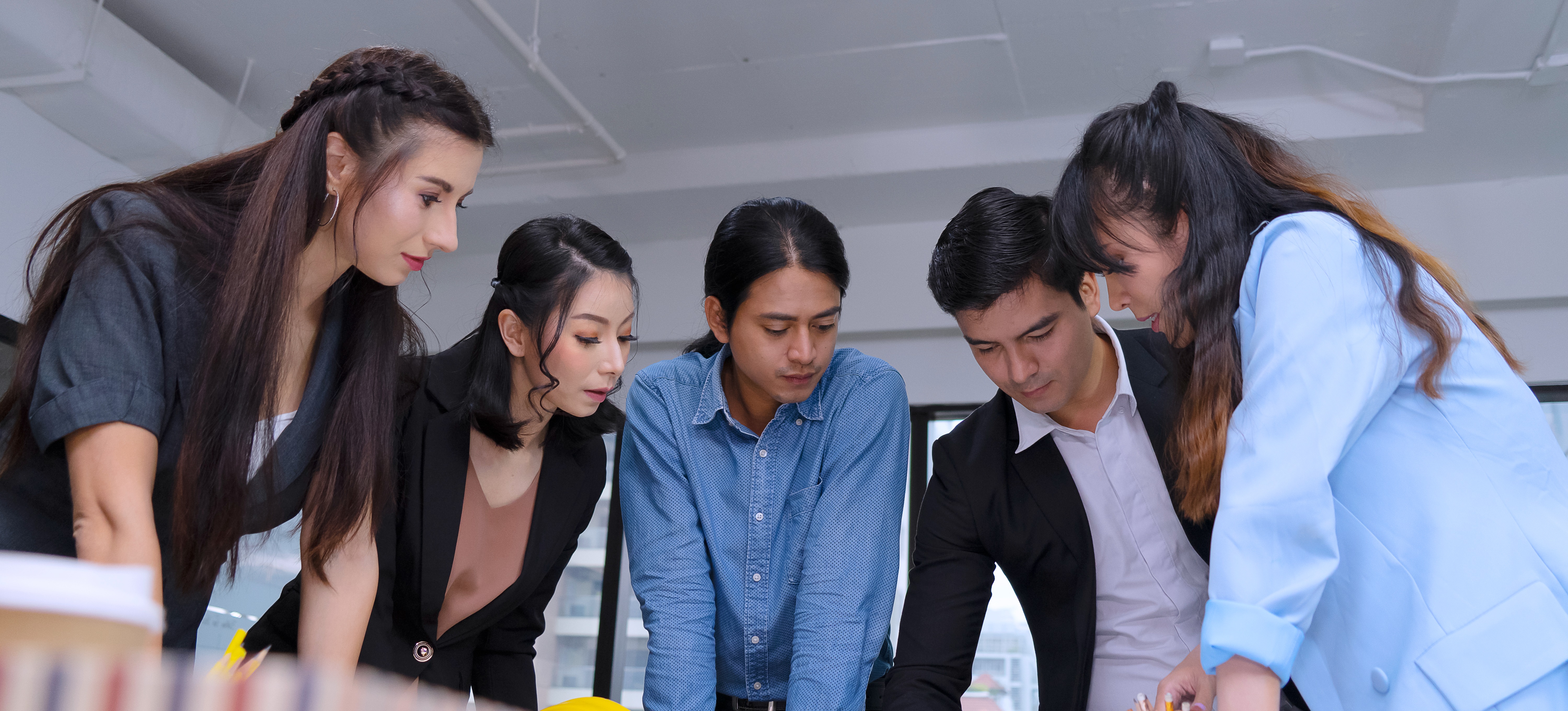 [Featured Image] A diverse team of business professionals stands over a table and creates a business continuity plan together.
