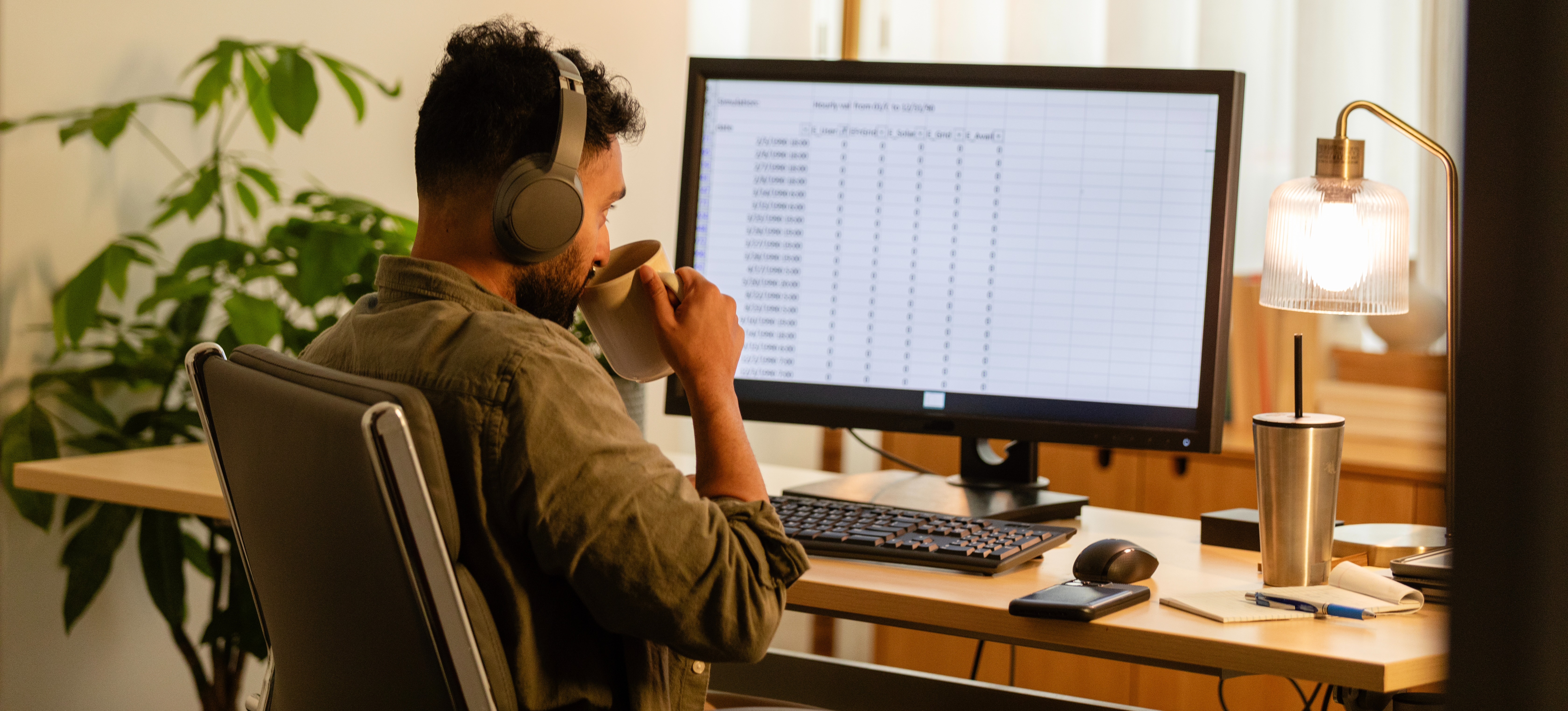 [Featured Image] A professional sips from a mug while wearing headphones and reviewing a spreadsheet after learning how to add a trendline in Google Sheets.