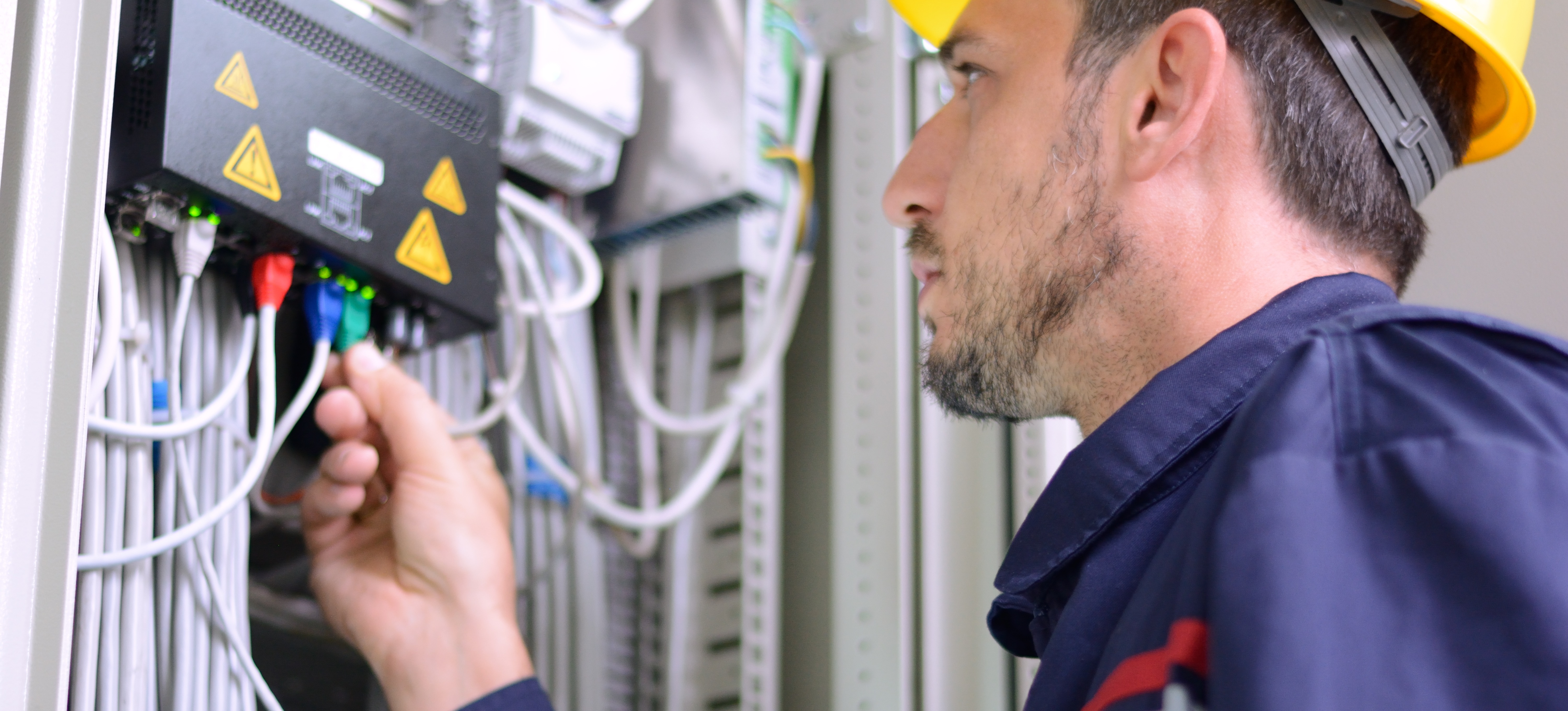 [Featured Image] A fiber technician connects fiber optic cables to a switch. 
