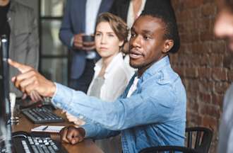 [Featured Image] A team leader points at his computer and talks with his coworkers about using artificial intelligence in UX design.