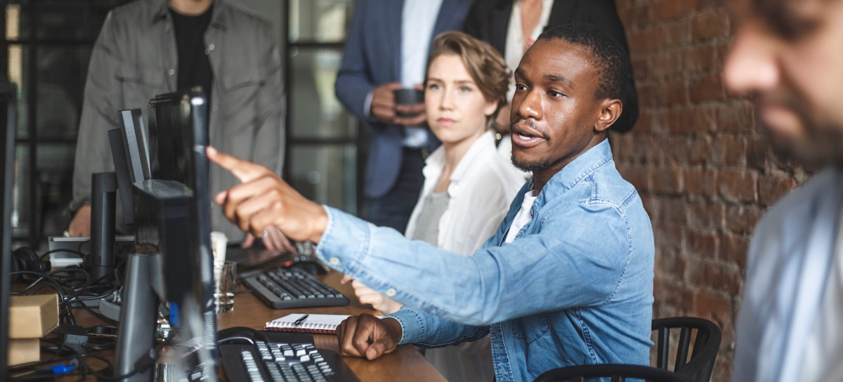 [Featured Image] A team leader points at their computer and talks with their coworkers about using artificial intelligence in UX design.