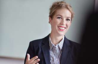 [Featured image] A female HR consultant, wearing a dark jacket and a blue striped shirt, is sitting at a table.