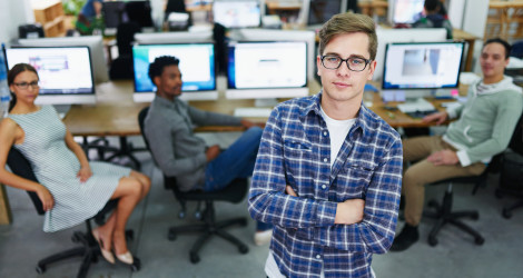 [Featured Image] A DevOps engineer in a blue button-down shirt stands in front of three members of his development team.