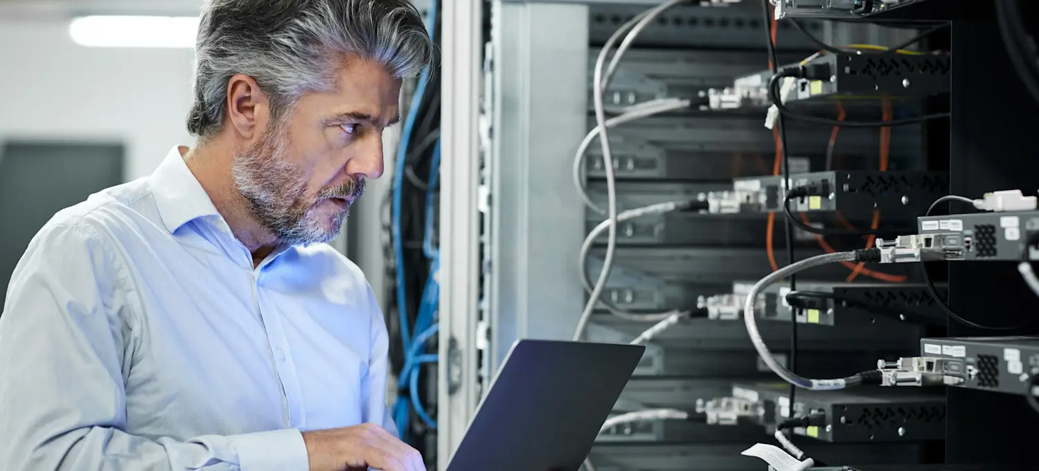[Featured Image] A technology analyst is in the server room of a client, creating a system to meet their operational needs.