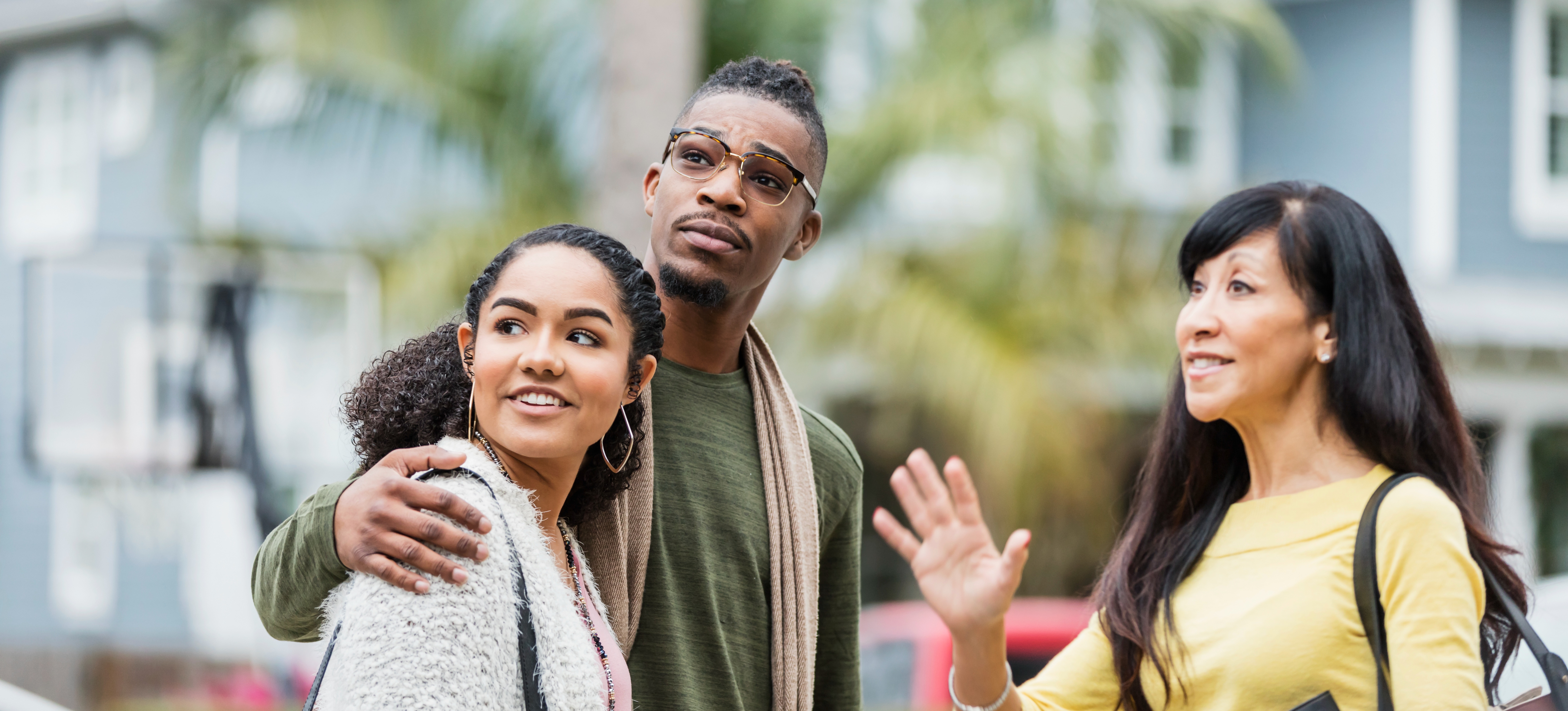[Featured image] A real estate agent is standing outside with a young couple showing them a home they might buy.
