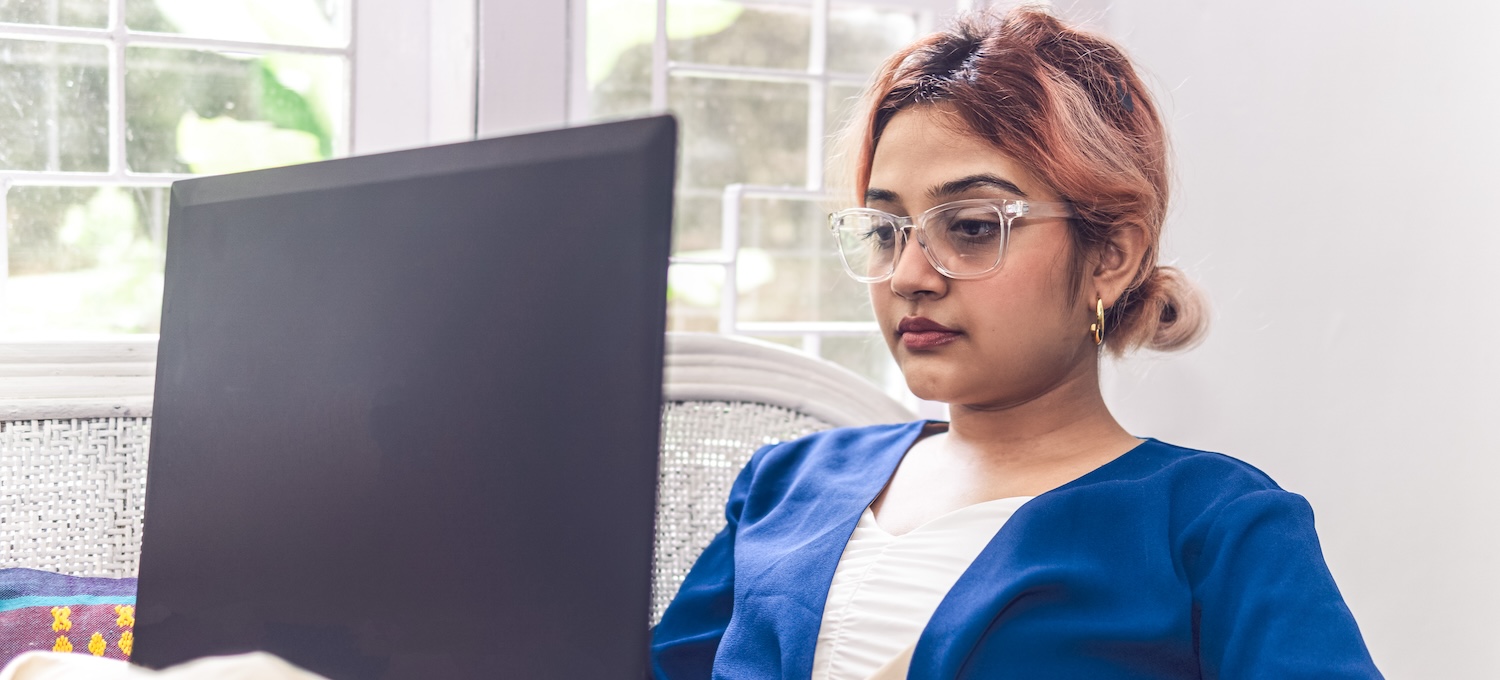 [Featured image] A woman with pink hair and glasses looks at her laptop, researching online completion degrees.