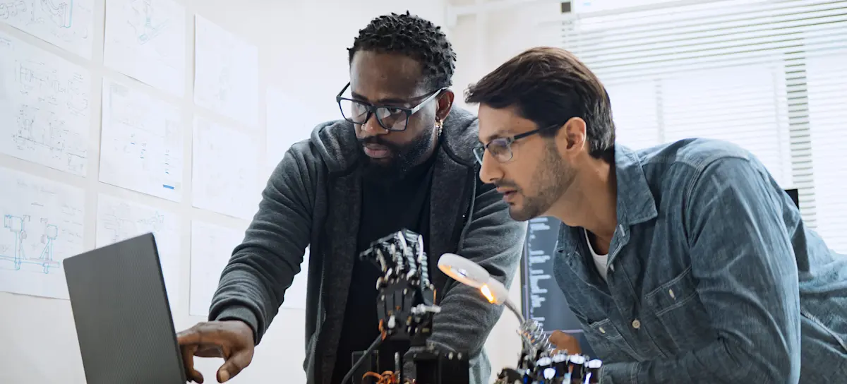 [Featured Image] Two computer programmers looking at a laptop screen and using AI to clean up paragraphs.
