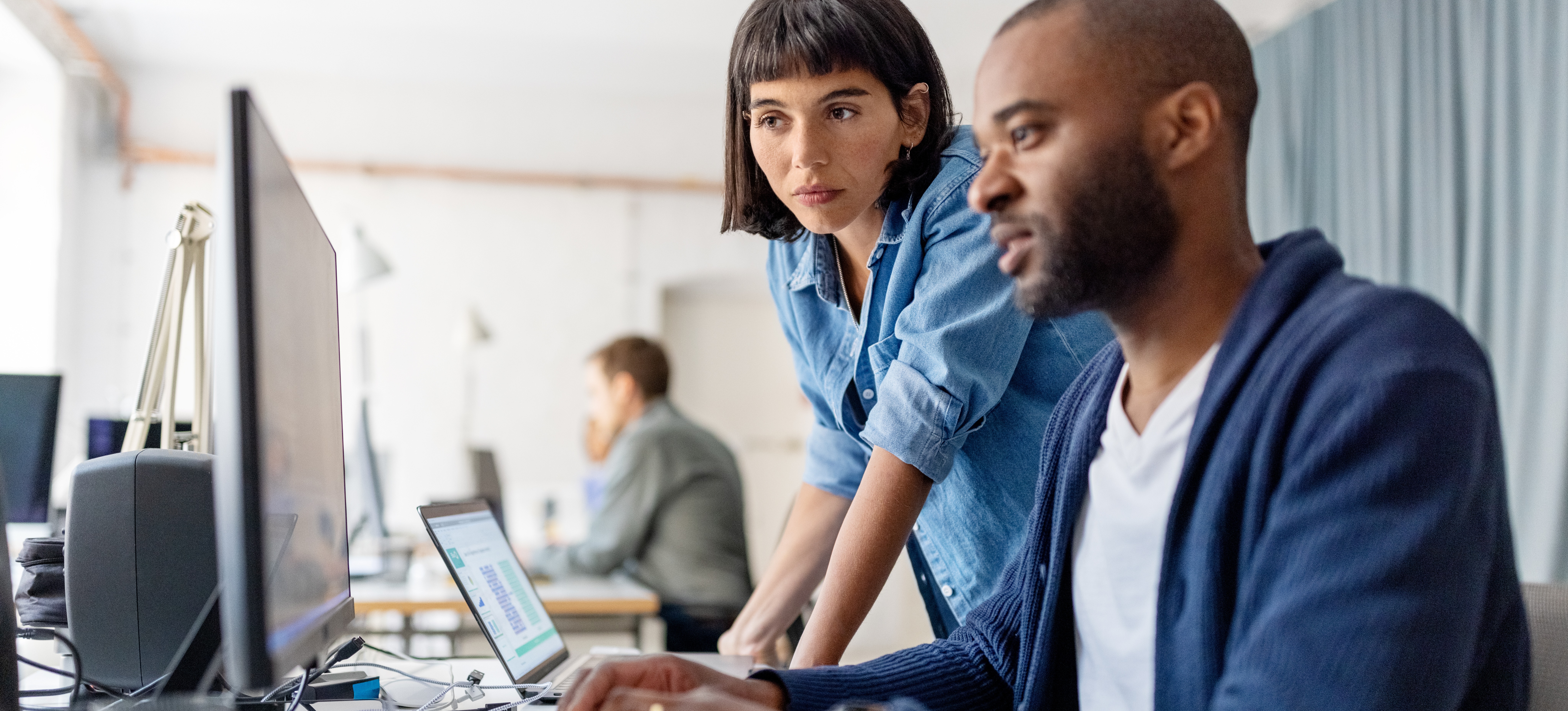 [Featured Image] Two coworkers are at a desk together, looking at the tableau programming language on a computer.
