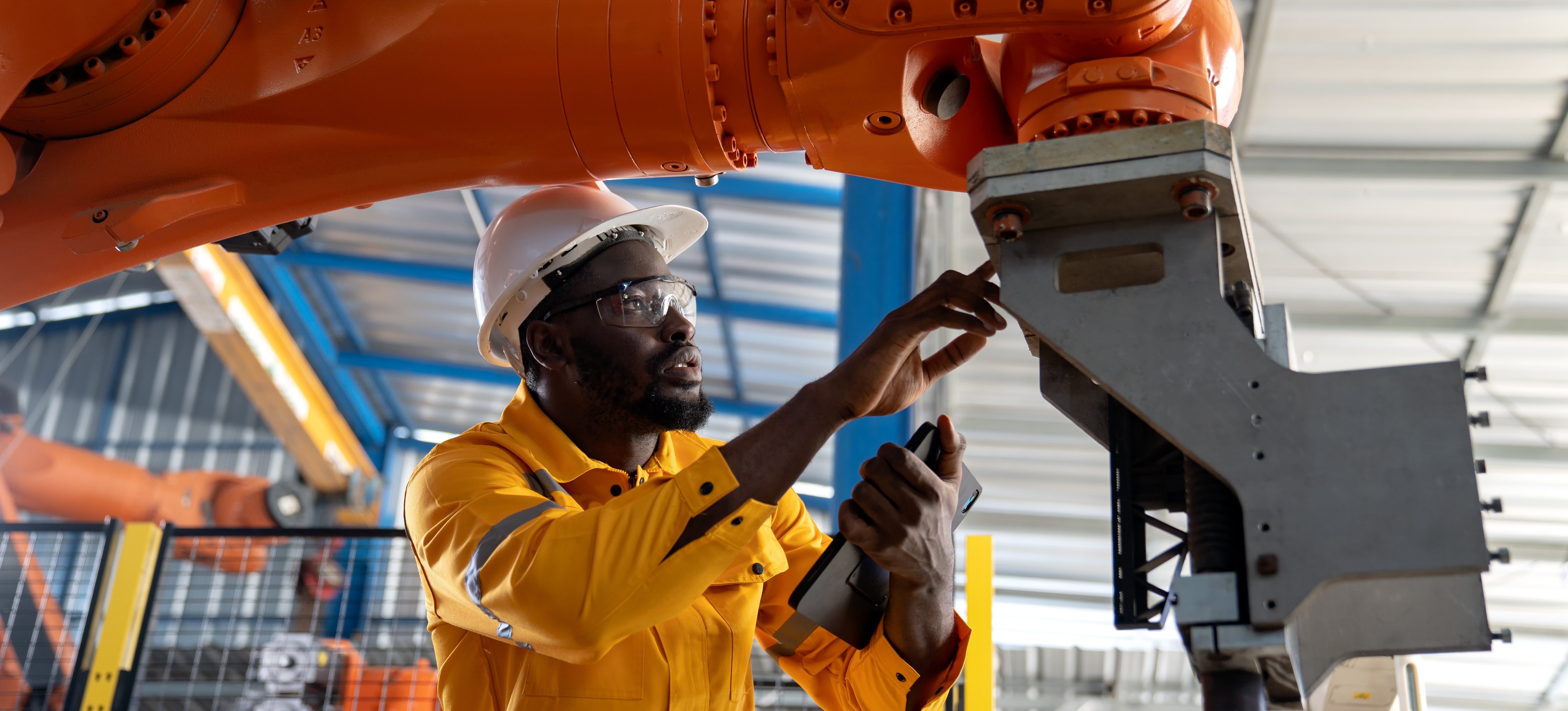 [Featured Image] An automation and control engineer programs welding parameters into an automated robot in a factory. 
