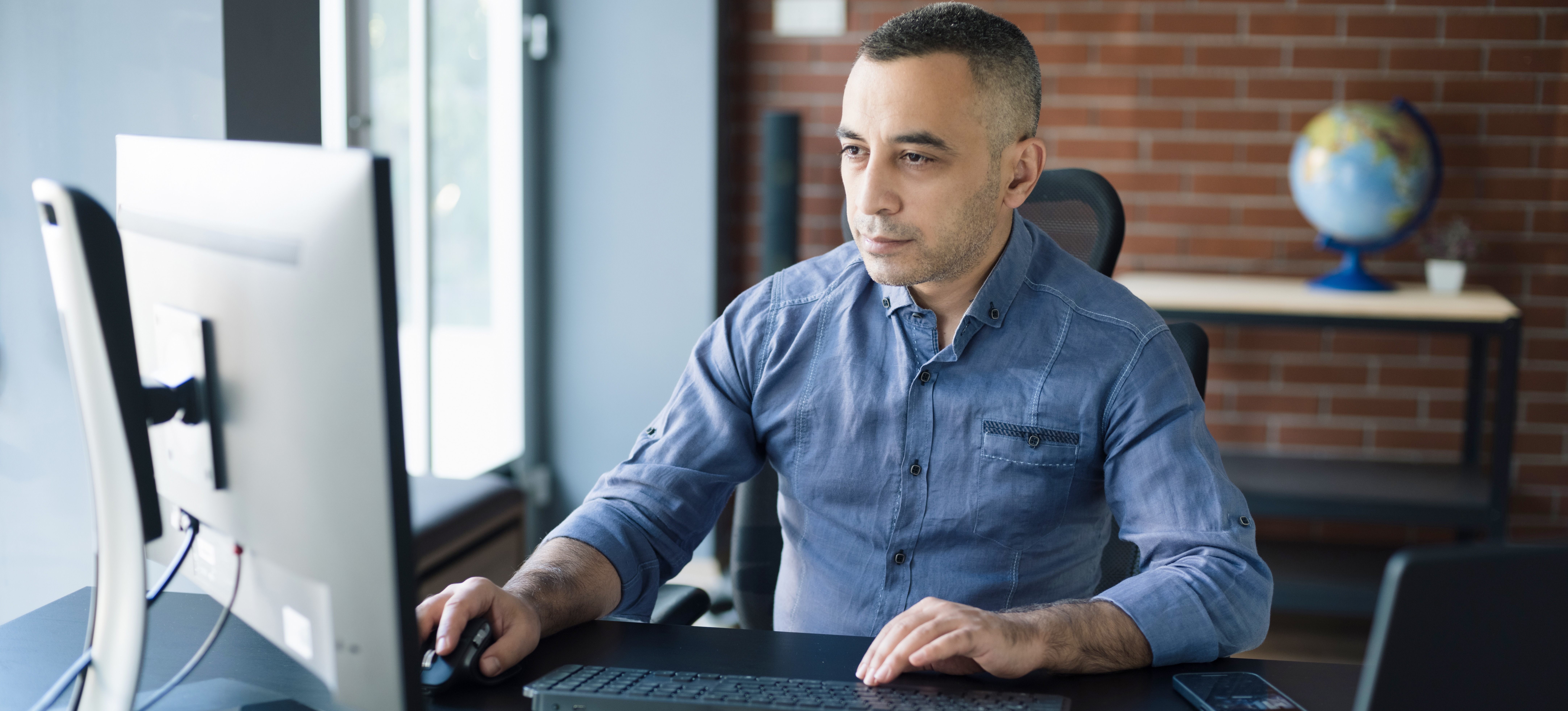 [Hauptbild] Ein Software-Ingenieur sitzt an einem Schreibtisch und arbeitet an seinem Computer. 