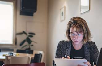 [Featured image]  A job seeker wearing a gray jacket, black top, and glasses looks for graphic design jobs on a tablet.