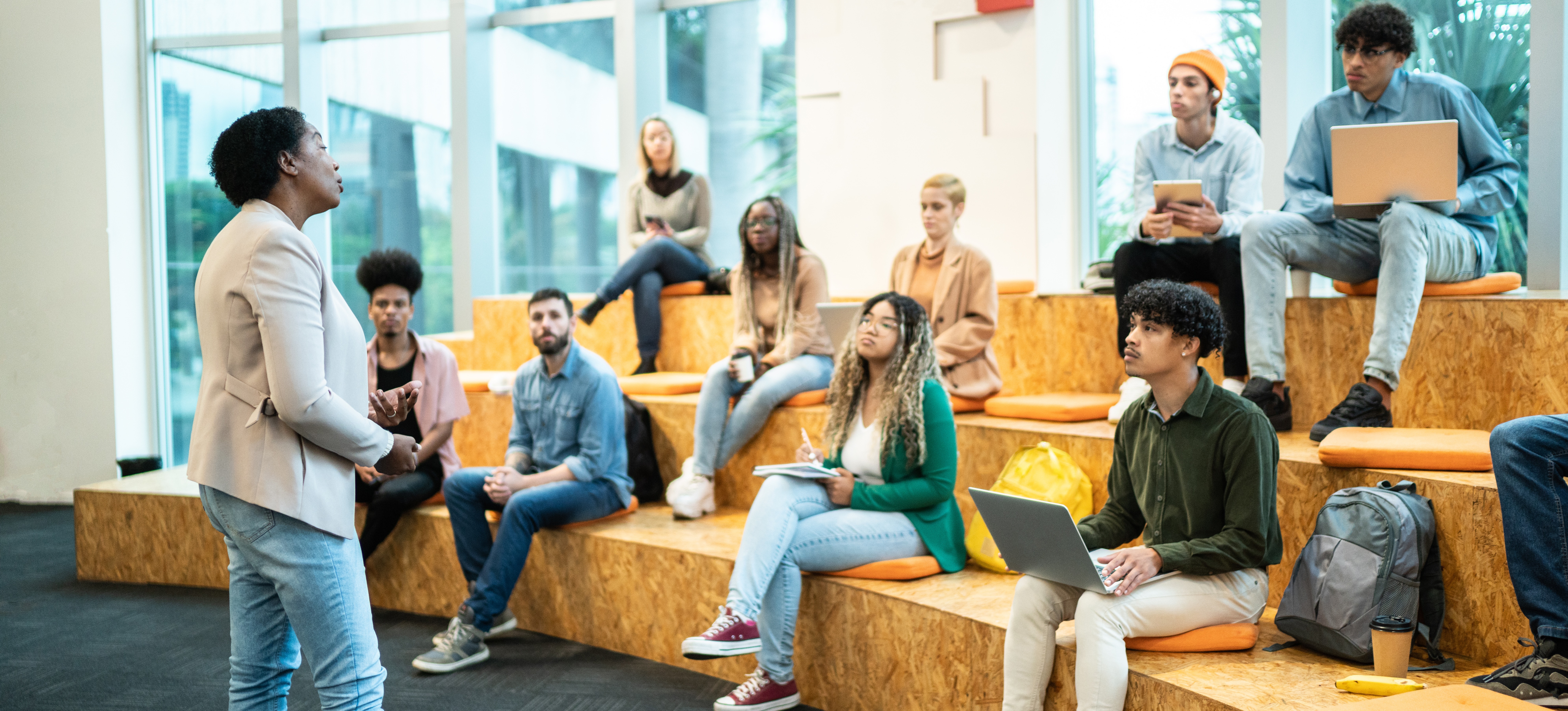 [Featured Image] A female teacher stands infront of a class in an open room explaining the gcse requirements for university.