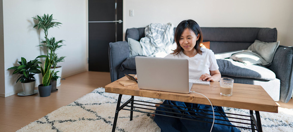 [Featured Image] A person in a white t-shirt sits on the floor at their coffee table and types prompts into ChatGPT for a project.