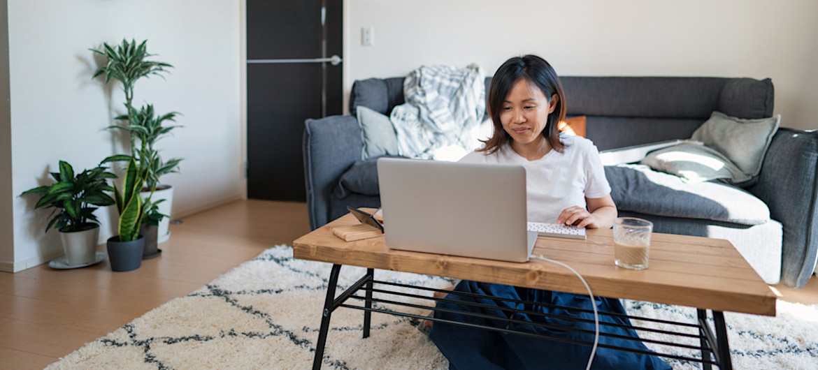 [Featured Image] A person in a white t-shirt sits on the floor at their coffee table and types prompts into ChatGPT for a project.