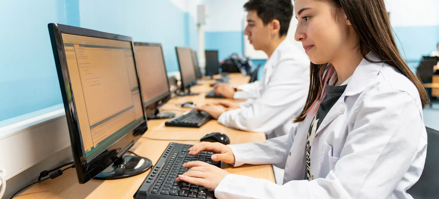 [Featured Image] A group of students work at computers in a college classroom while working towards their master's in data science.