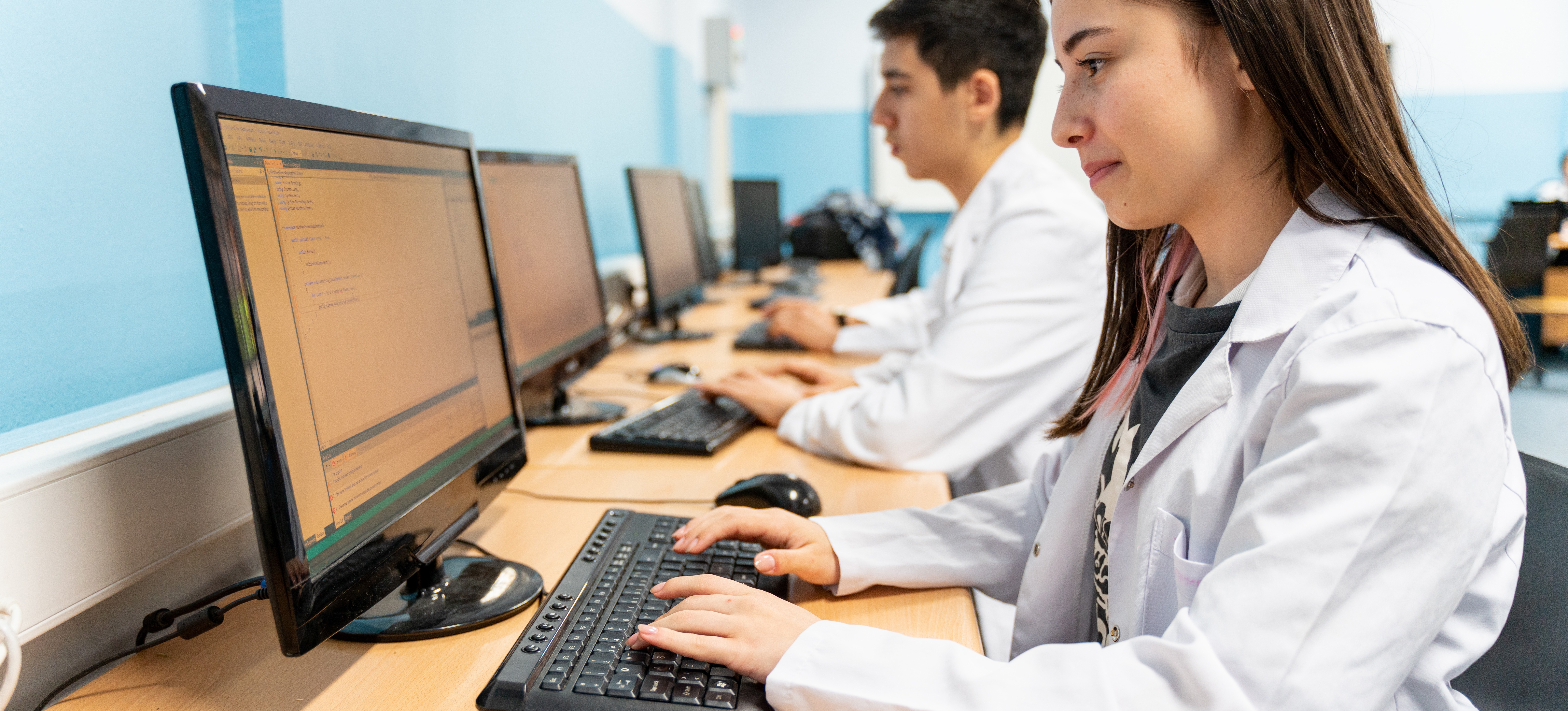[Featured Image] A group of students work at computers in a college classroom while working towards their master's in data science.