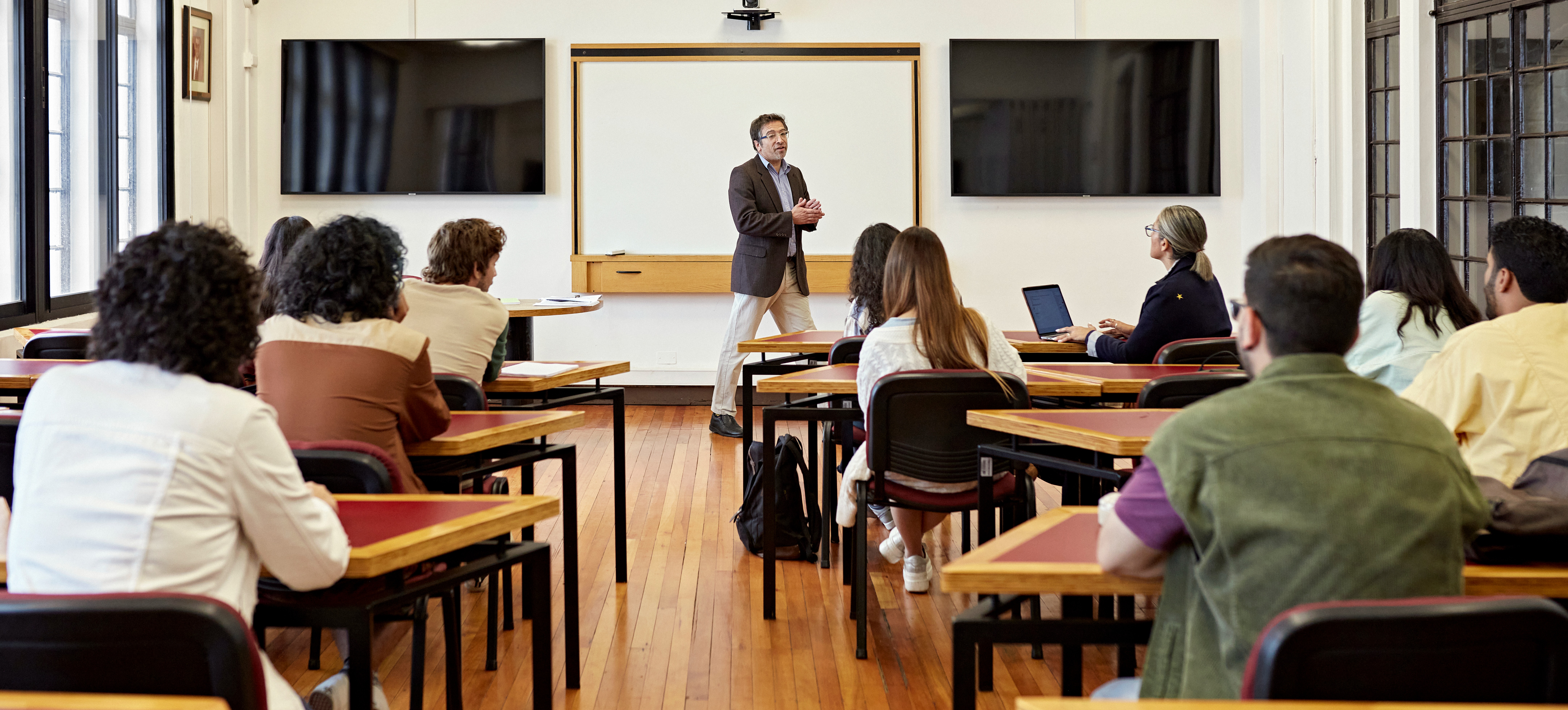 [Featured Image] A male teacher stands infront of a college class and is teaching "What is typography".