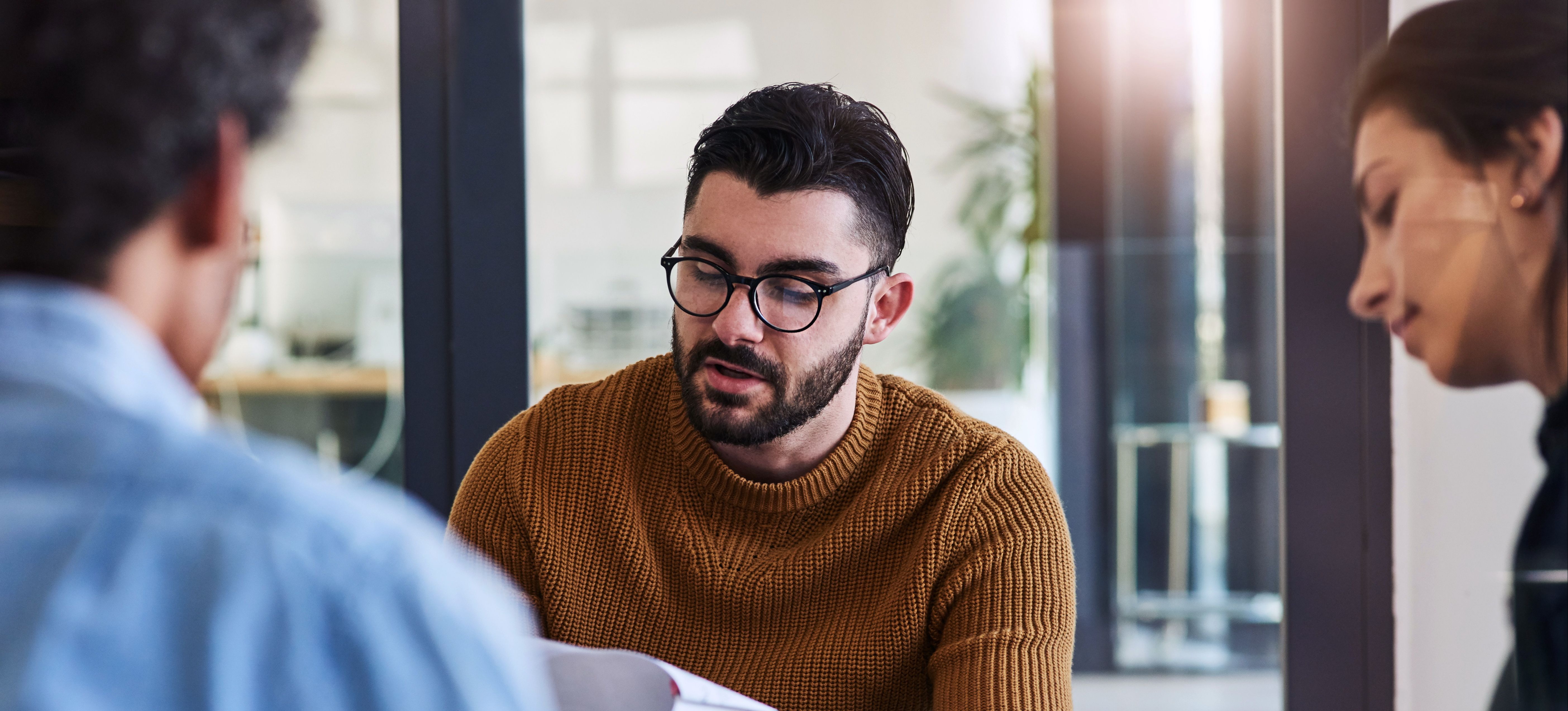 [Featured Image] Three coworkers are sitting in a circle looking at papers of practice interview questions. 
