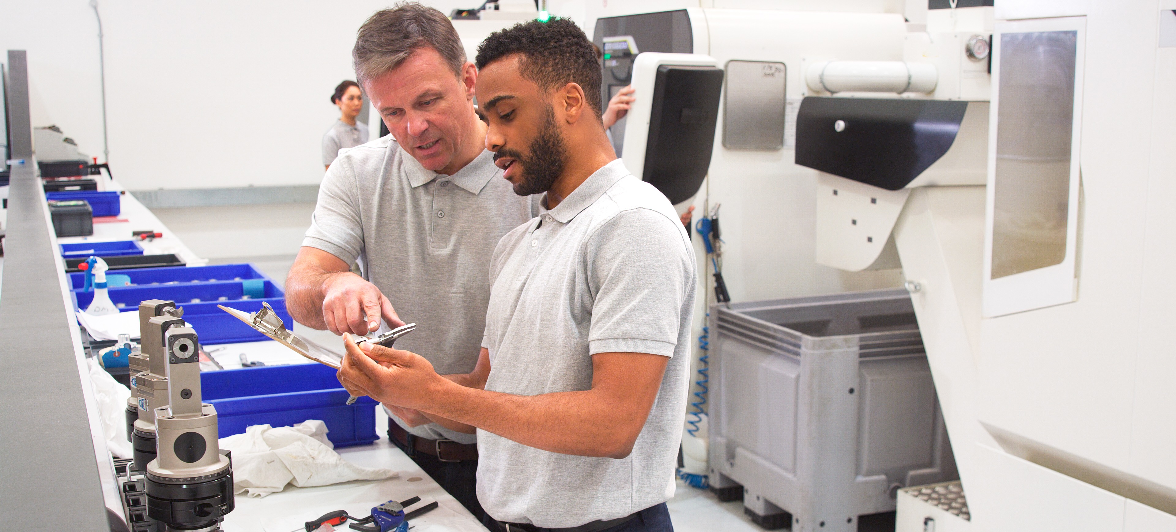 [Featured Image] A mentor stands next to an apprentice in a medical apprenticeship program and explains lab results.
