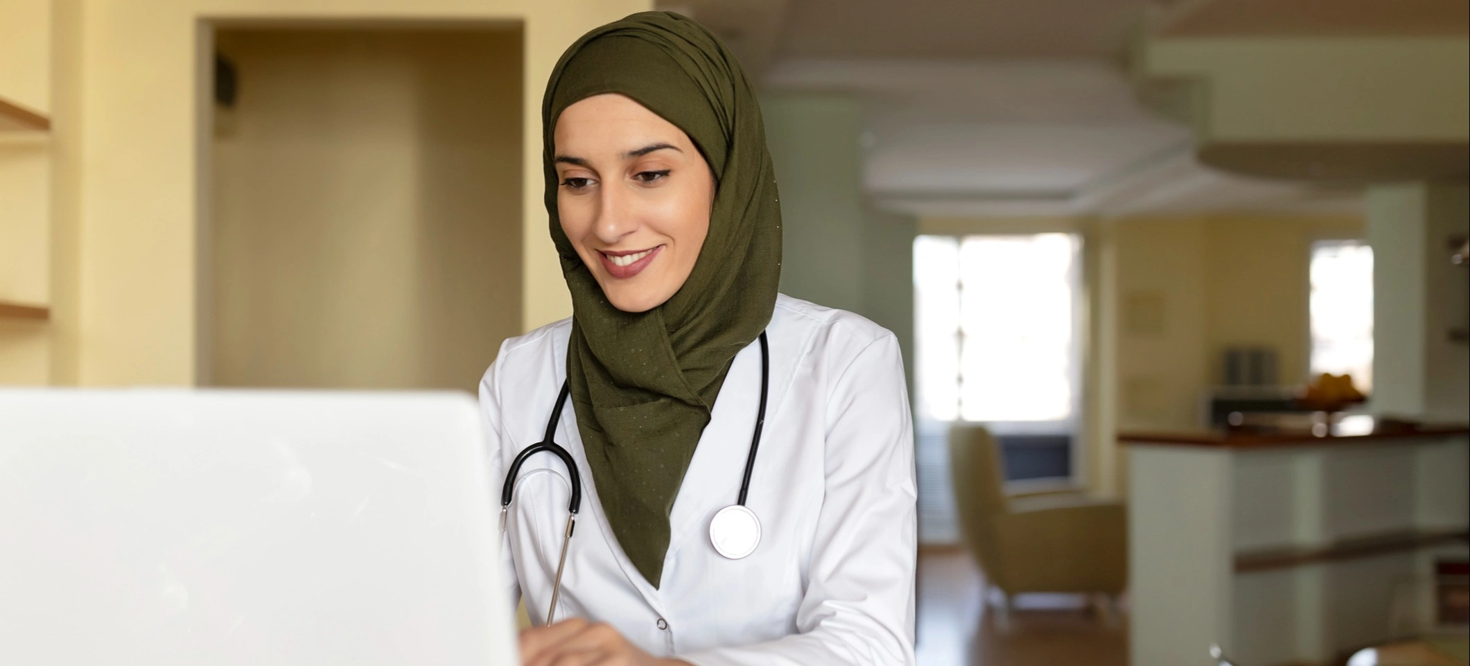 [Featured image] A surgeon in a white coat and stethoscope checks files in front of a computer monitor.