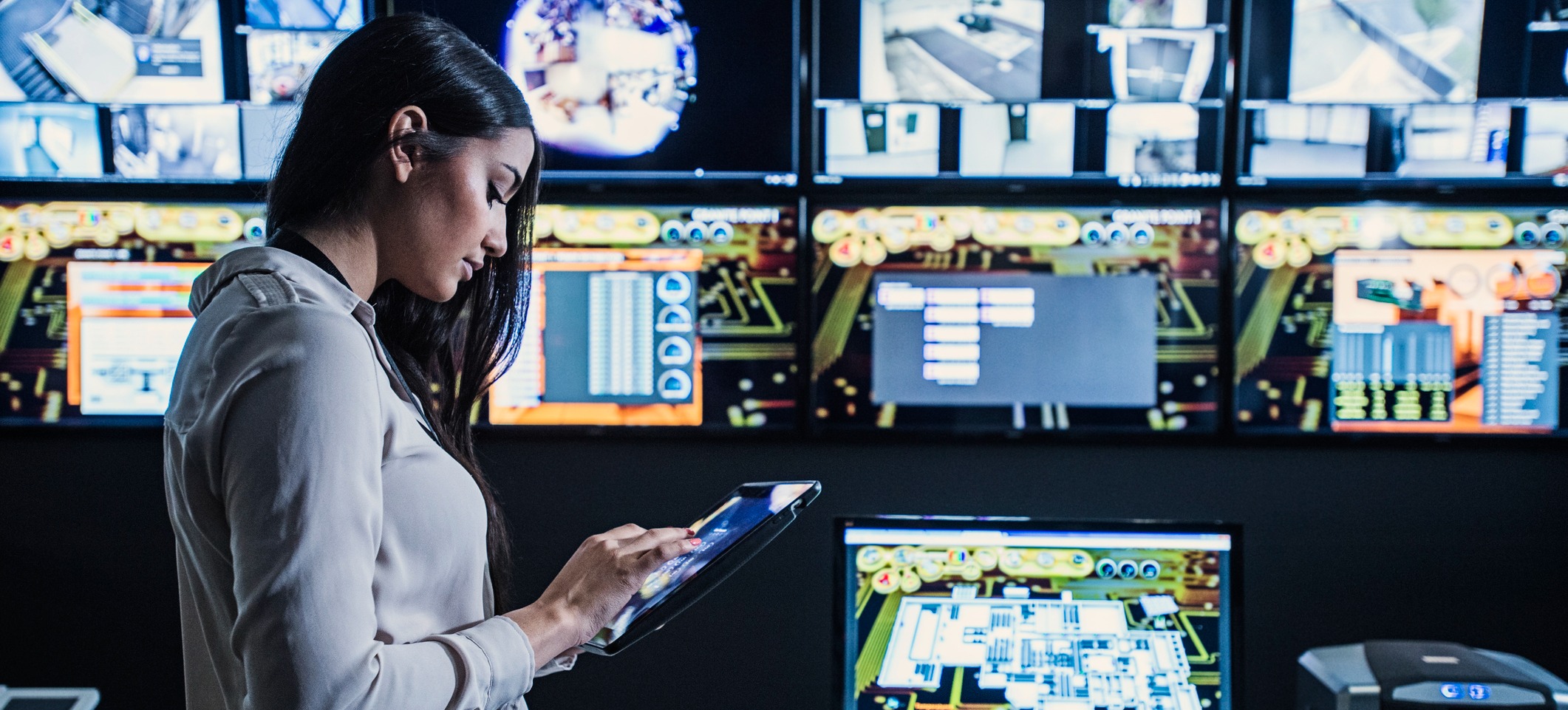 [Featured Image] A person looks at their tablet with computers surrounding them.