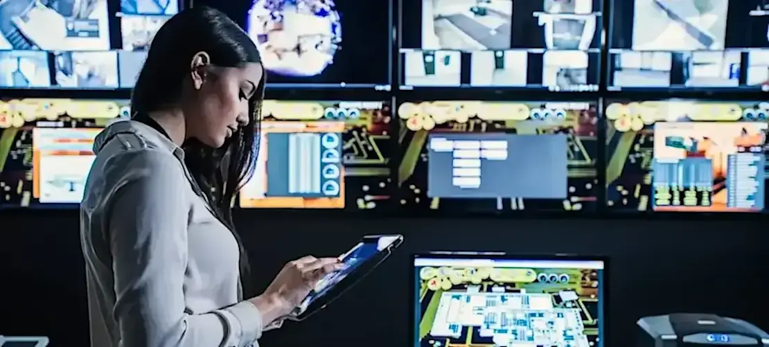 [Featured Image] A person looks at their tablet with computers surrounding them.