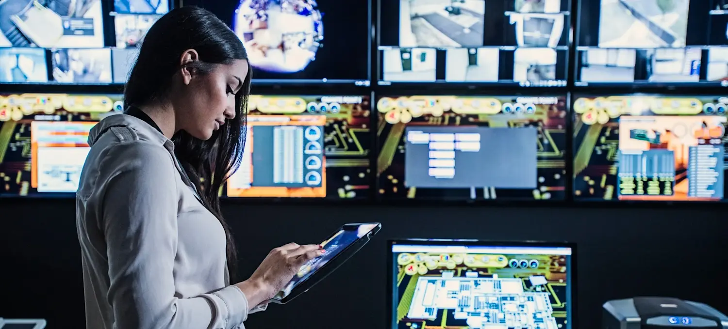 [Featured Image] A person looks at their tablet with computers surrounding them.
