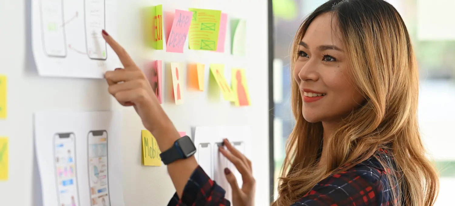 [Featured Image] A UX designer points to a mockup of an app design made using low-fidelity wireframe tools.
