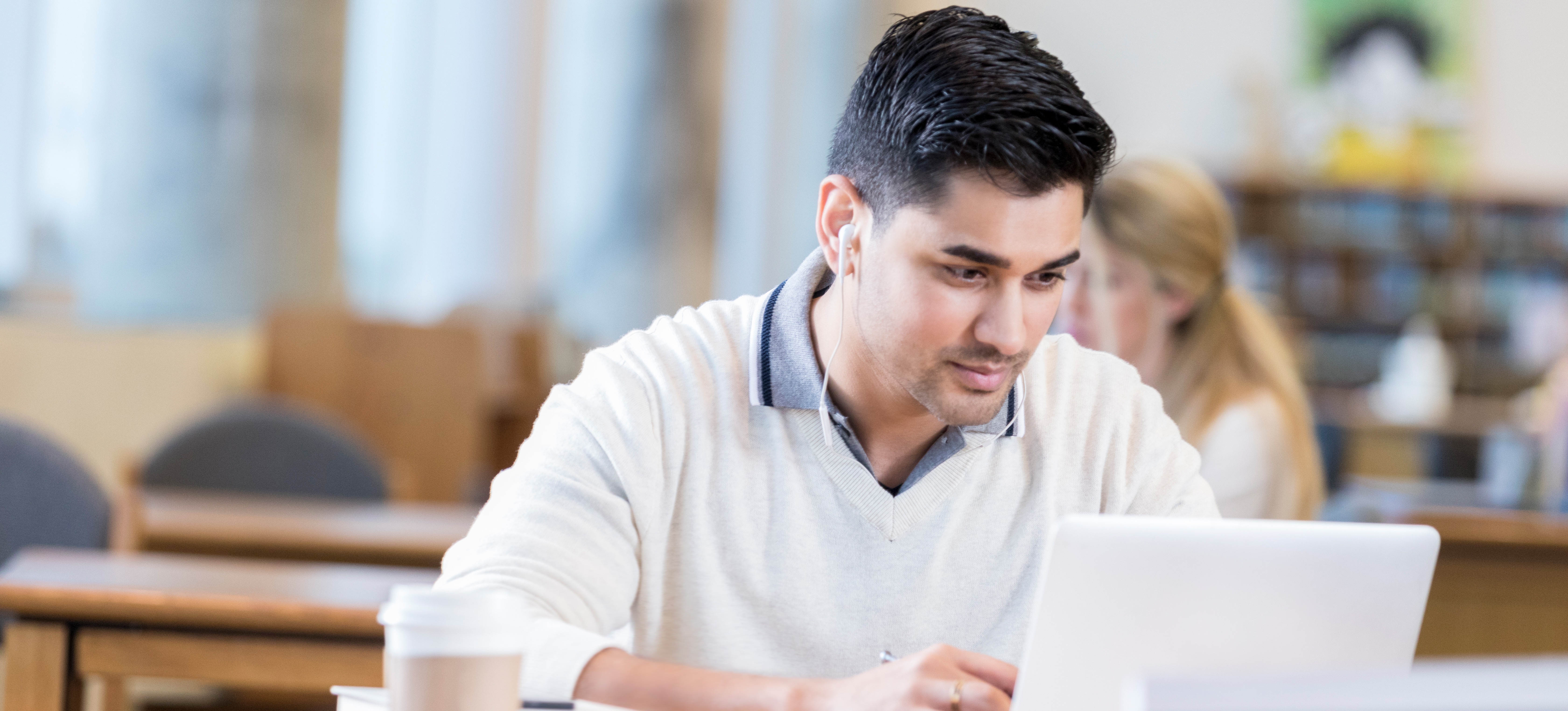 [Featured Image] A young  learner uses a laptop in a library to research what the difference is between BE and BTech. 
