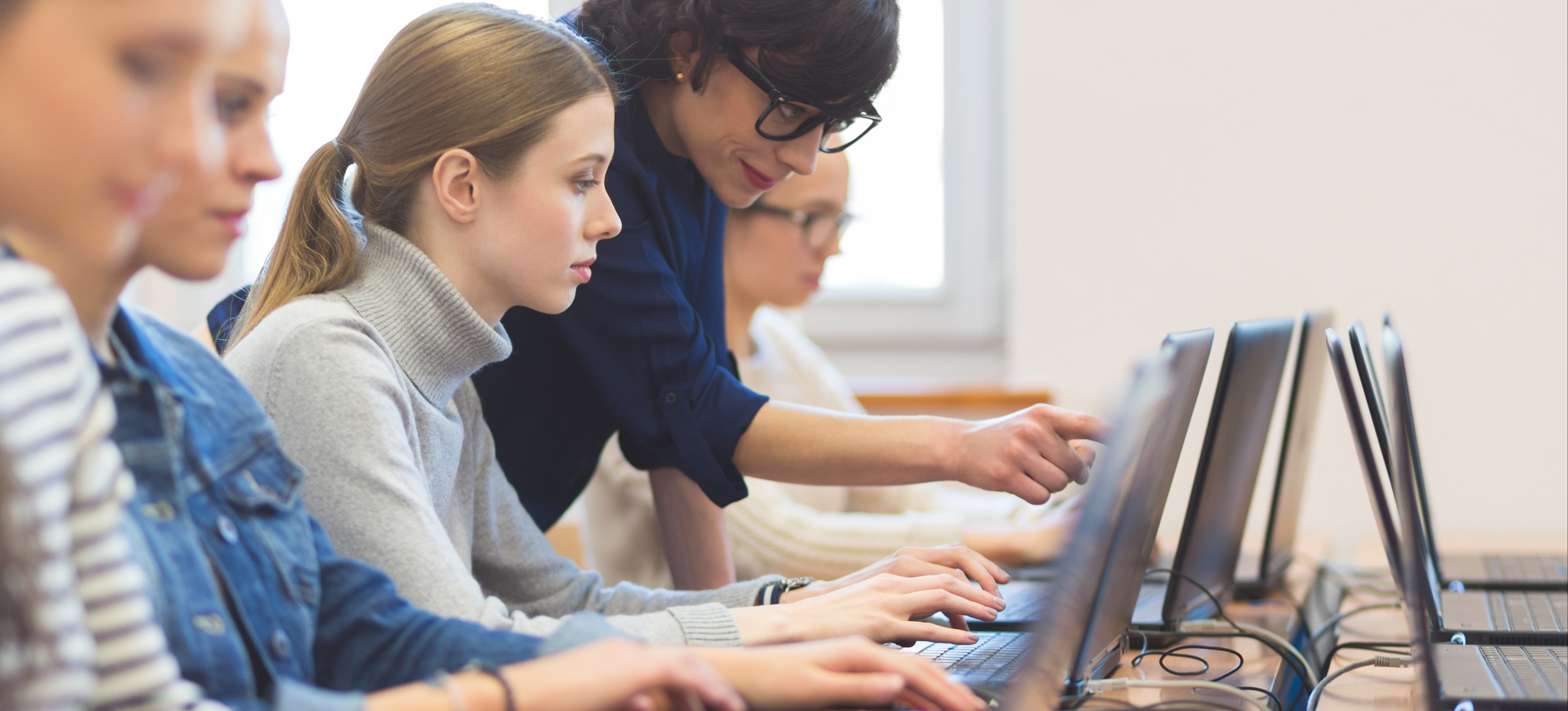 [Featured Image] Learners in an IT classroom, learning about IT auditing and information systems, with an instructor discussing the importance of CISA certification.