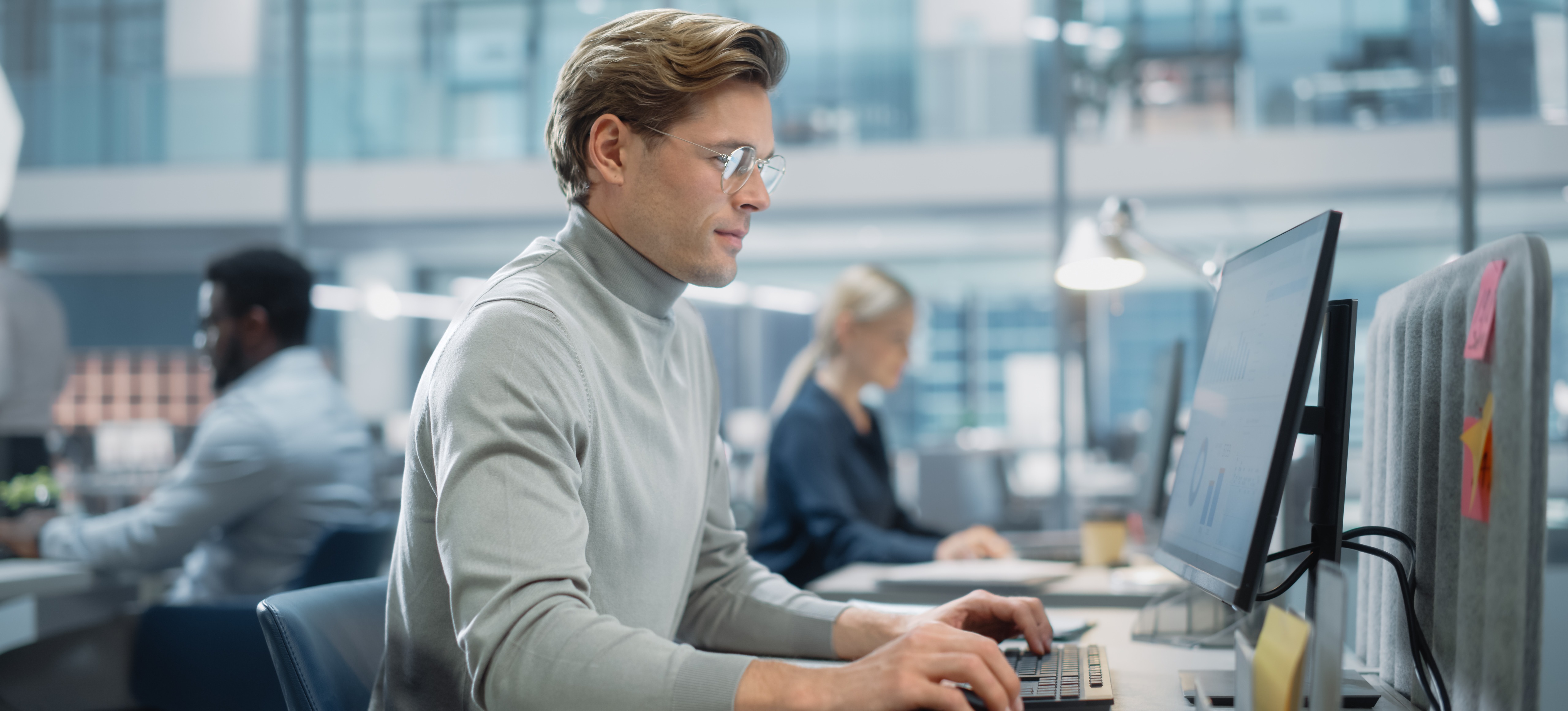 [Featured Image] A machine learning engineer sits at his computer in an office workstation near their colleagues and is working with embedding models.
