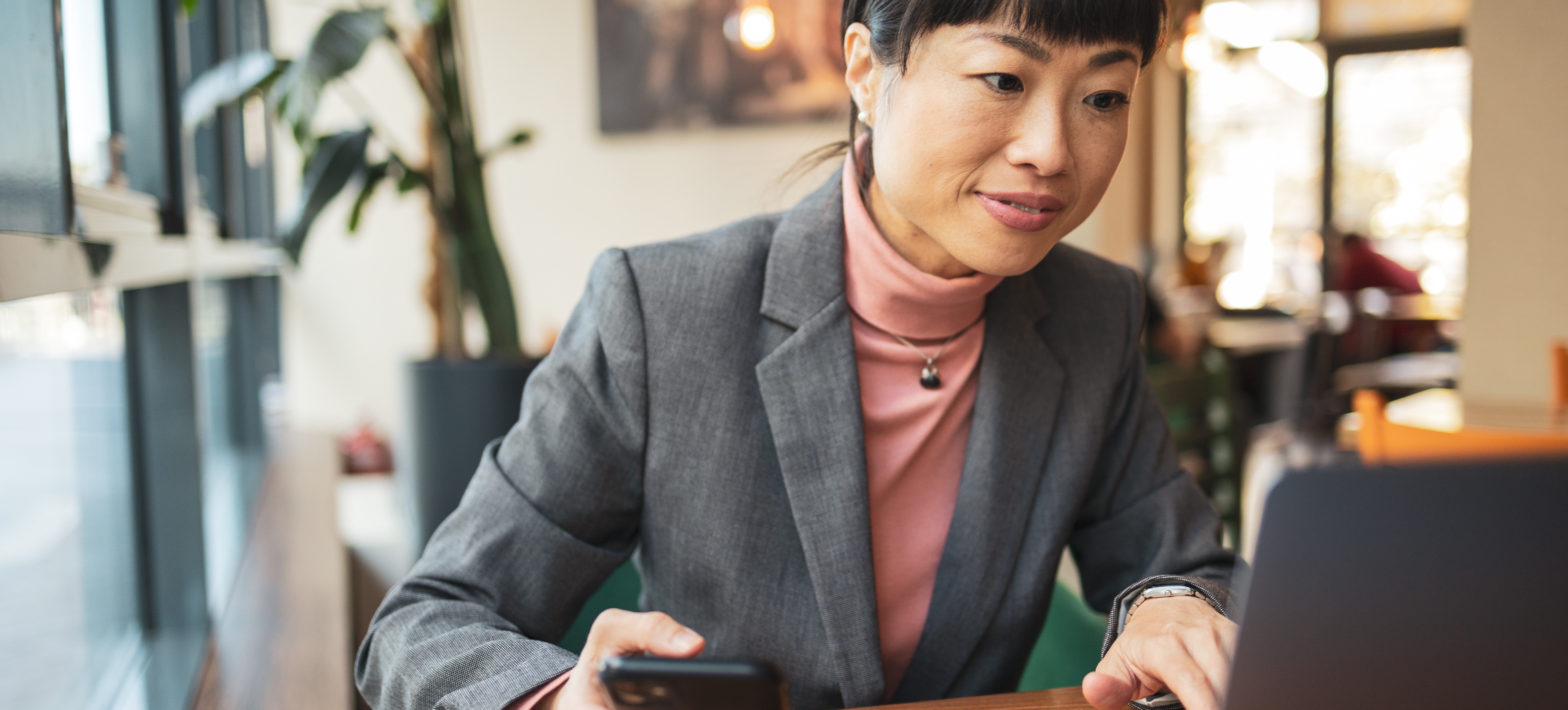 [Featured image] Business woman using her mobile phone as multifactor authentication to login on her computer.
