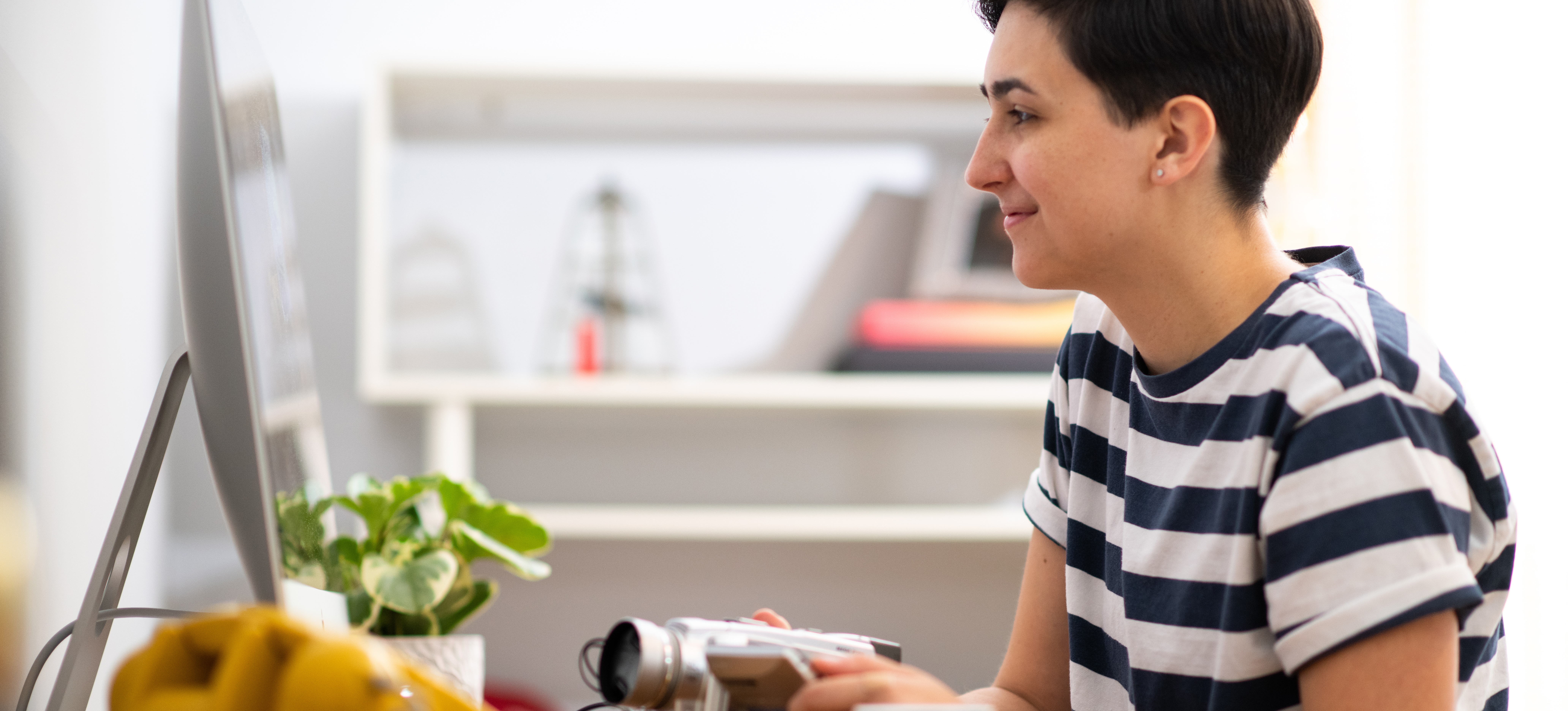[Featured Image] A person is using AI video editing tools while sitting at a wooden desk with a video camera in hand. 
