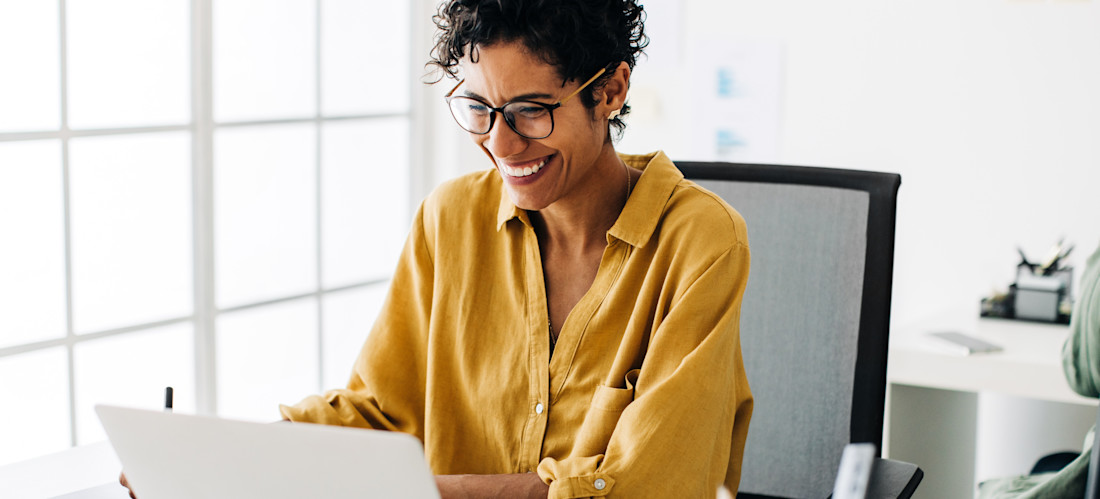 [Featured Image] A human resources employee sits at their desk and uses an HRIS on their laptop. 
