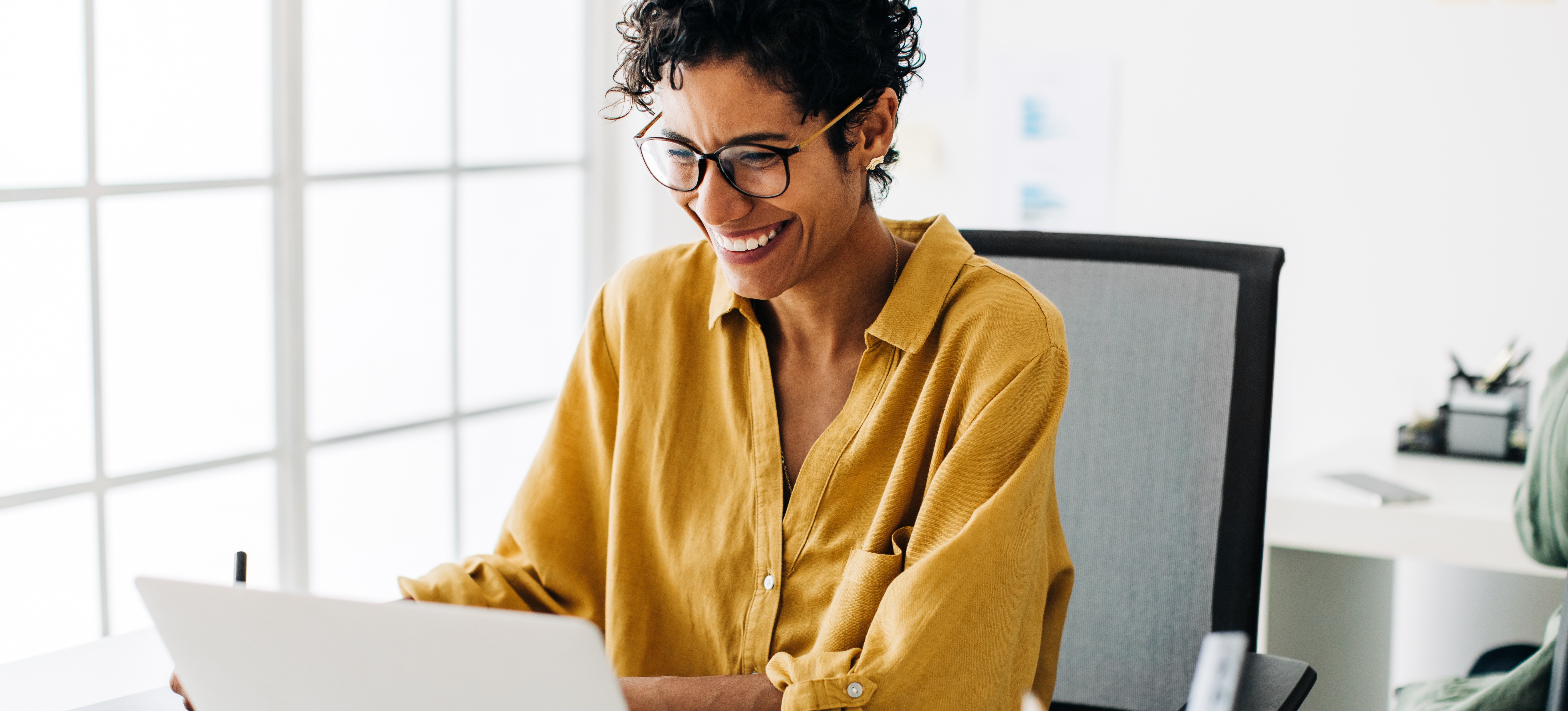 [Featured Image] A human resources employee sits at their desk and uses an HRIS on their laptop. 
