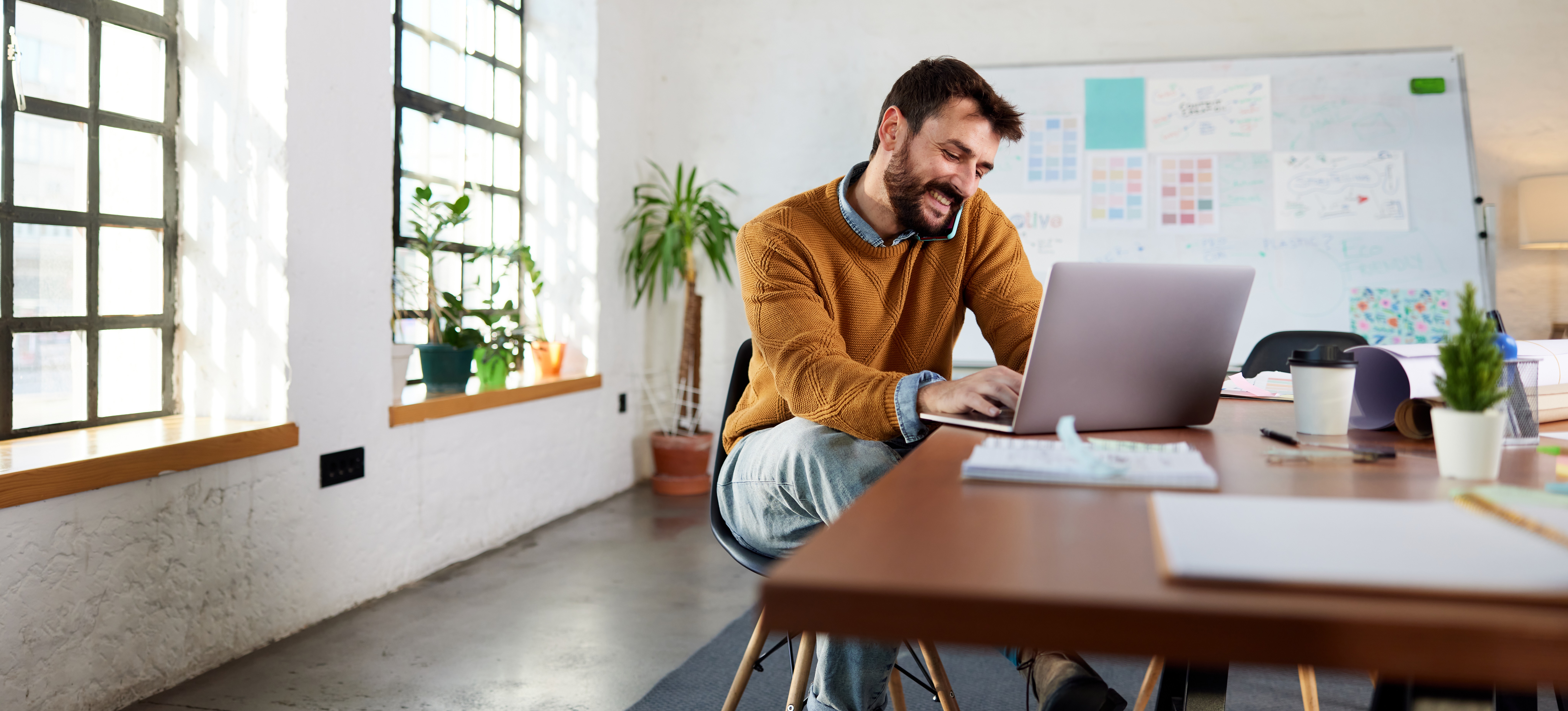 [Featured Image] A product owner speaks on the phone and works on their laptop while preparing a presentation for the development team to use while meeting with stakeholders.
