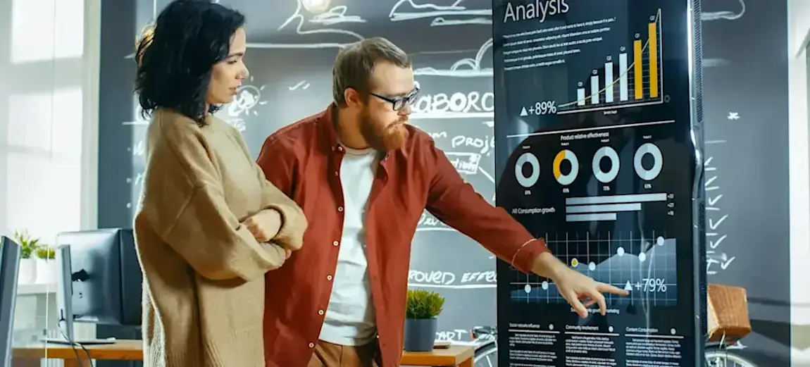 [Featured Image] Two workers discuss statistical modeling while looking at data on a chart.