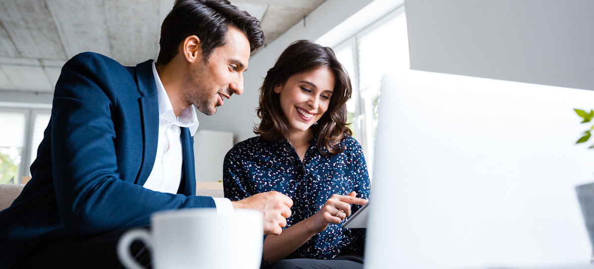 [Hauptbild] Zwei Personen, die an einer Affiliate-Marketing-Kampagne arbeiten, arbeiten gemeinsam an einem Schreibtisch mit einem Tablet und einem Laptop.