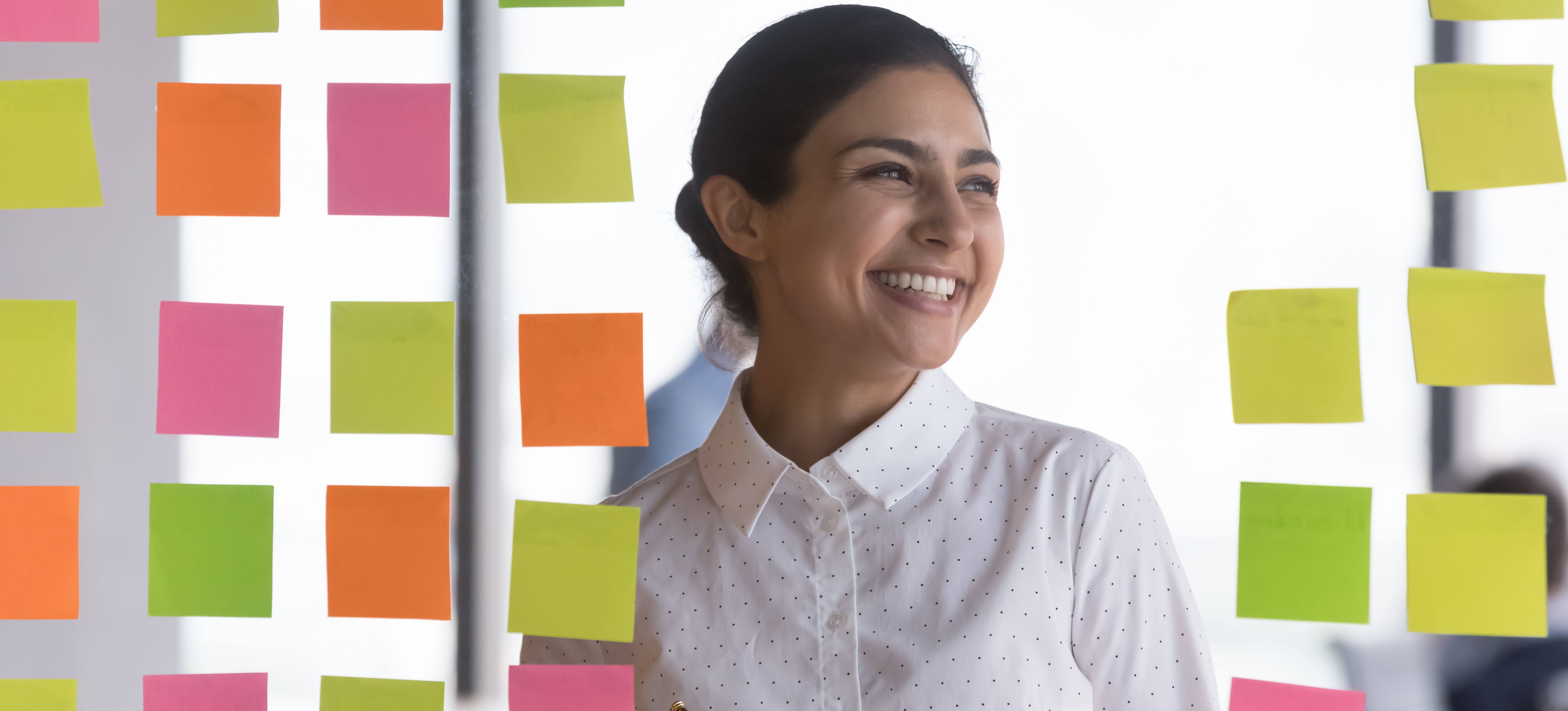 [Hauptbild] Eine lächelnde Geschäftsfrau arbeitet an ihrem Kanban-Board, das sie in Verbindung mit einiger der besten Projektmanagement-Software verwendet.
