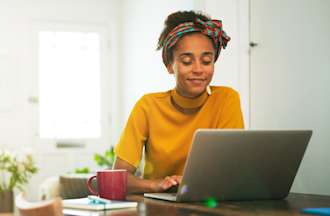 [Featured Image] A woman works on a laptop at a living room table.