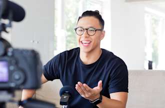 [Featured Image] Man with top bun and round glasses speaks in front of a camera in his living room.