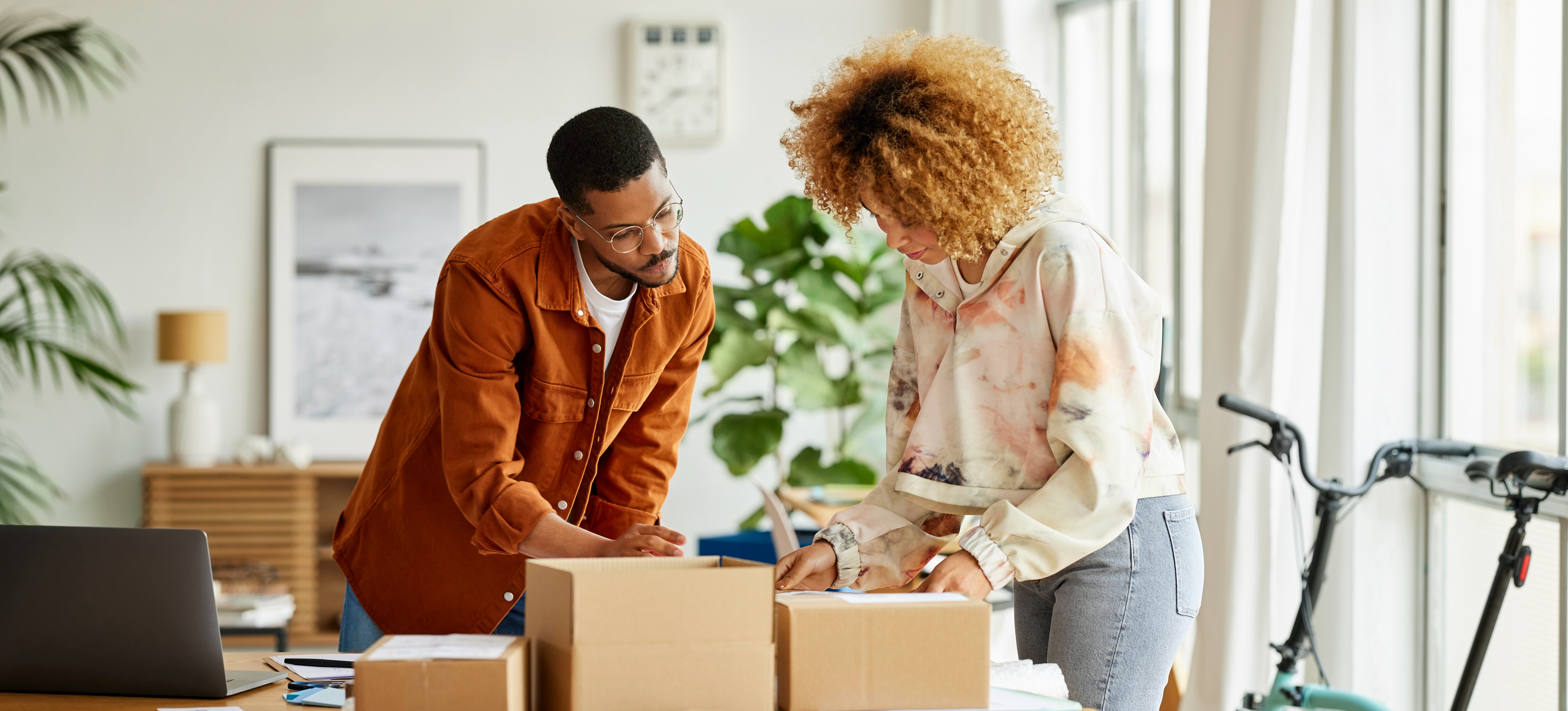 [Hauptbild] Zwei Mitarbeiter beraten sich beim Verpacken von Bestellungen und diskutieren, wie sich die Einhaltung von E-Commerce-Trends auf das Geschäft ausgewirkt hat.