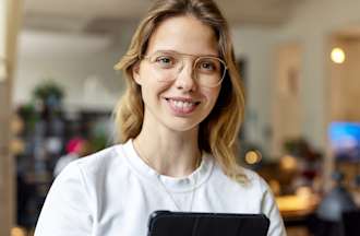 [Featured image] An Azure-certified professional stands in an office holding a tablet while smiling. 