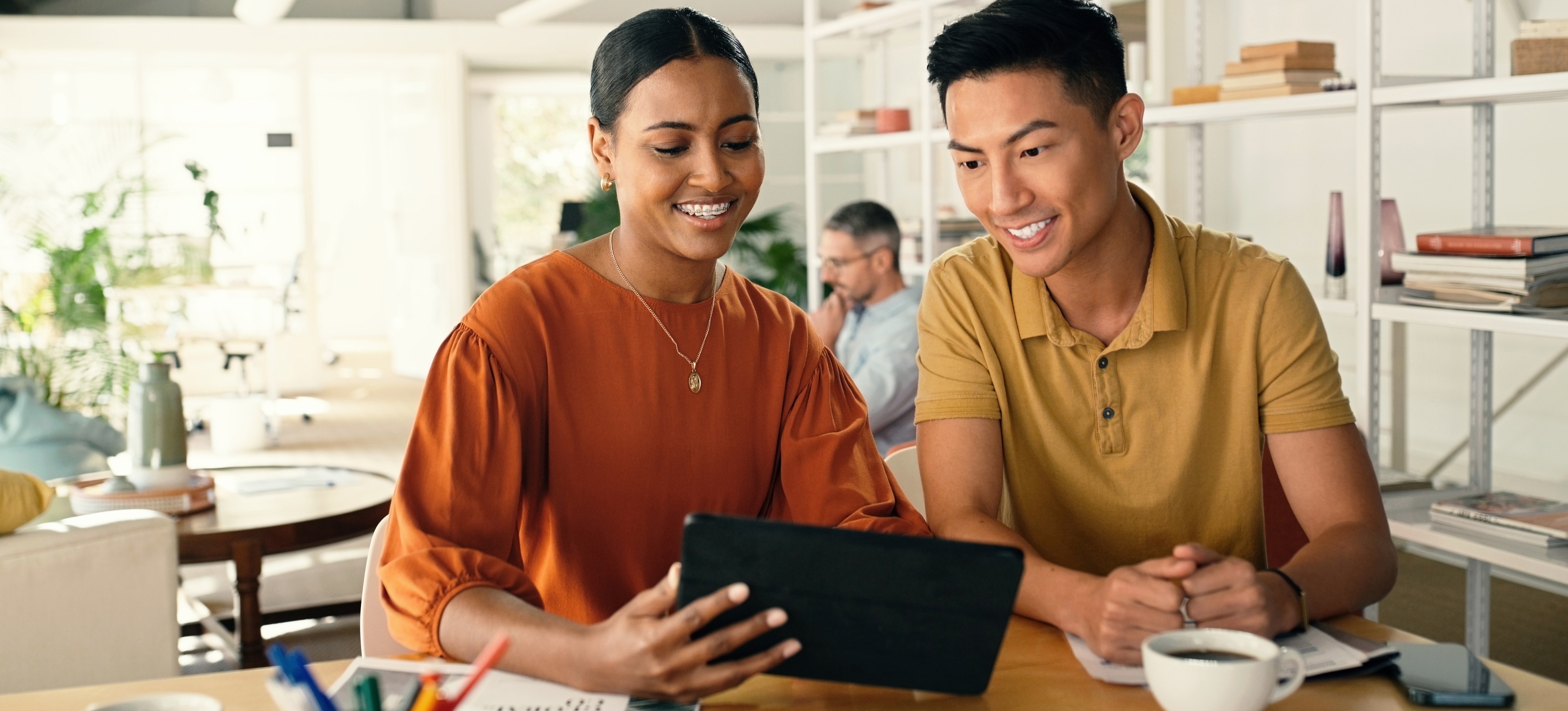 [Featured Image] Two colleagues look at a tablet and discuss what graphic design is and how to incorporate it into their marketing campaign. 