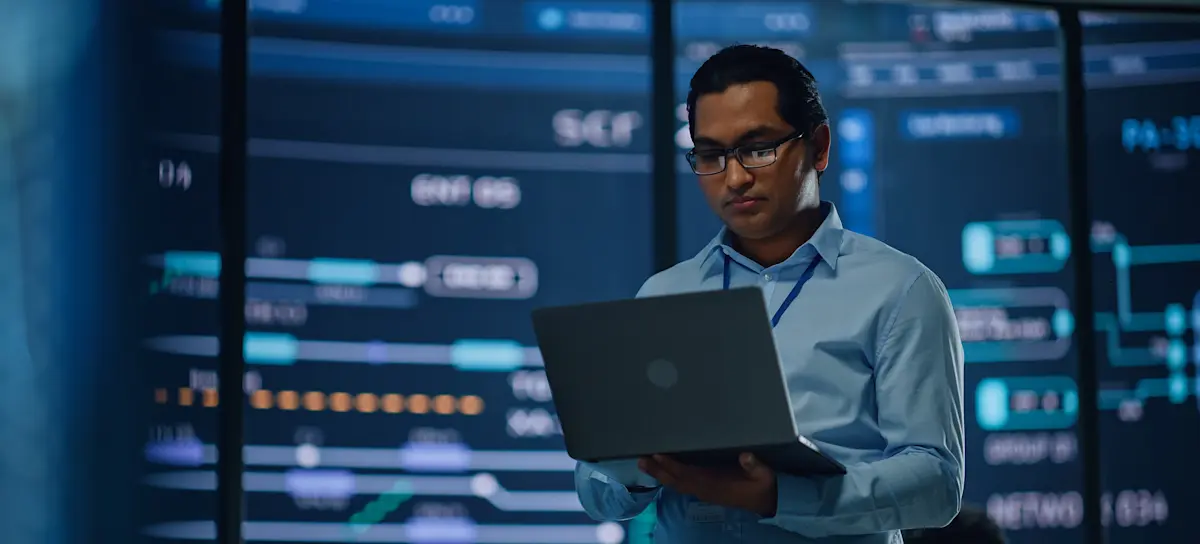[Featured Image] A person stands in a room full of servers examining a hypervisor on a laptop computer.
