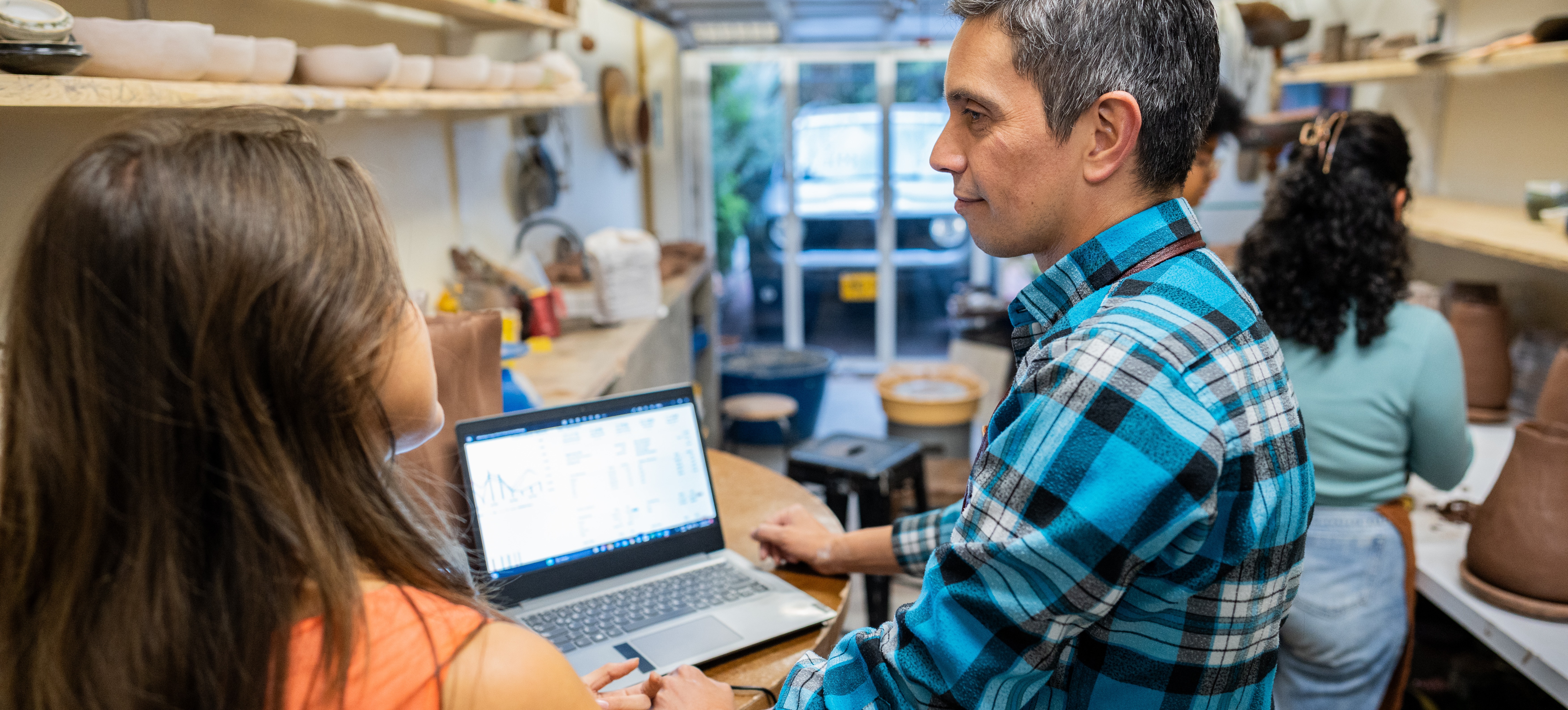 [Featured Image] A ceramics store owner stands with colleagues in his shop in front of his laptop and learns how to use Google Merchant feed product_type.