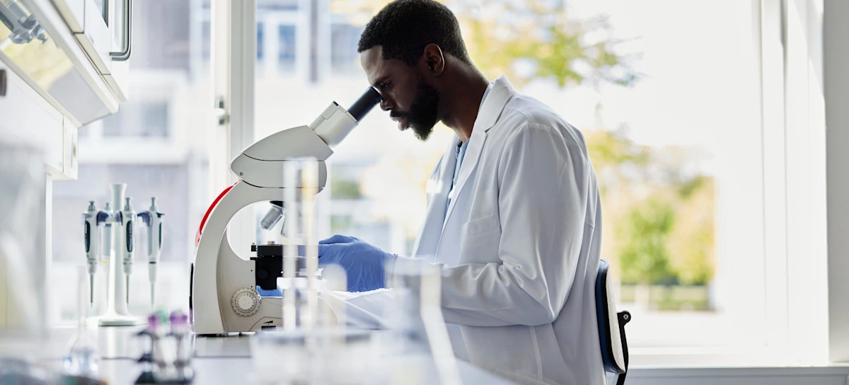 [Featured Image] An epidemiologist, one of many Power BI jobs that rely on data visualization, looks into a microscope in a lab.
