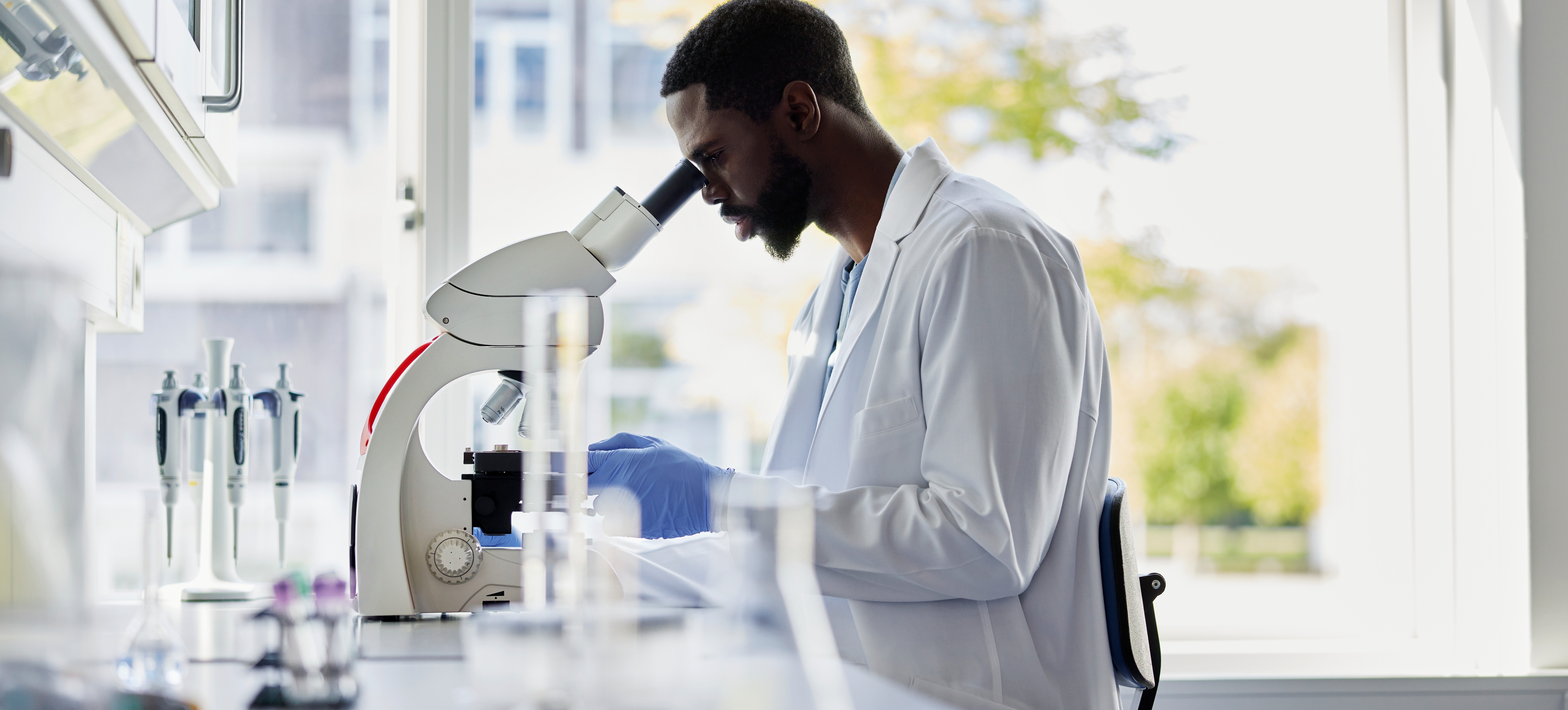 [Featured Image] An epidemiologist, one of many Power BI jobs that rely on data visualization, looks into a microscope in a lab.
